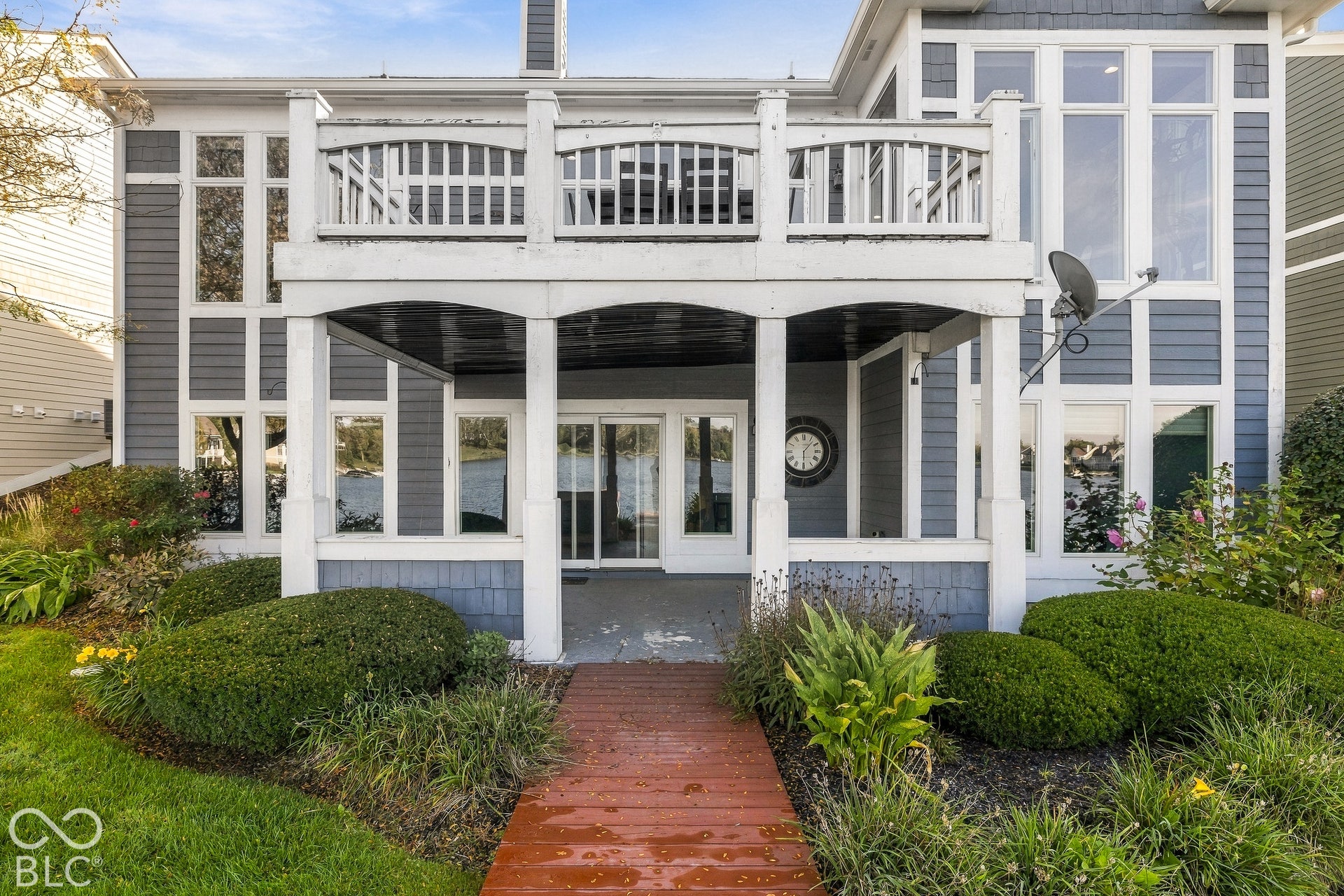 Two-story exterior featuring blue siding with white trim, a covered lower-level patio, an elevated balcony, and large picture windows