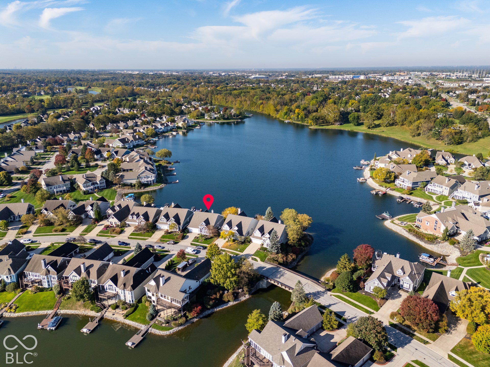Aerial perspective of waterfront property featuring direct lake access, a private boat dock, multi-level architectural design, and surrounding mature tree-lined landscapes