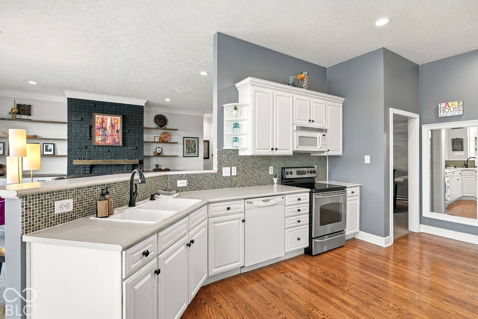 Kitchen featuring white cabinetry, solid-surface countertops, tile backsplash, stainless steel appliances, and wood-finish flooring