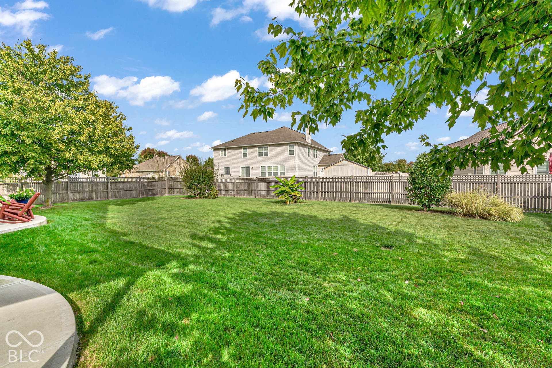Expansive backyard featuring a manicured lawn, established trees, and a concrete patio