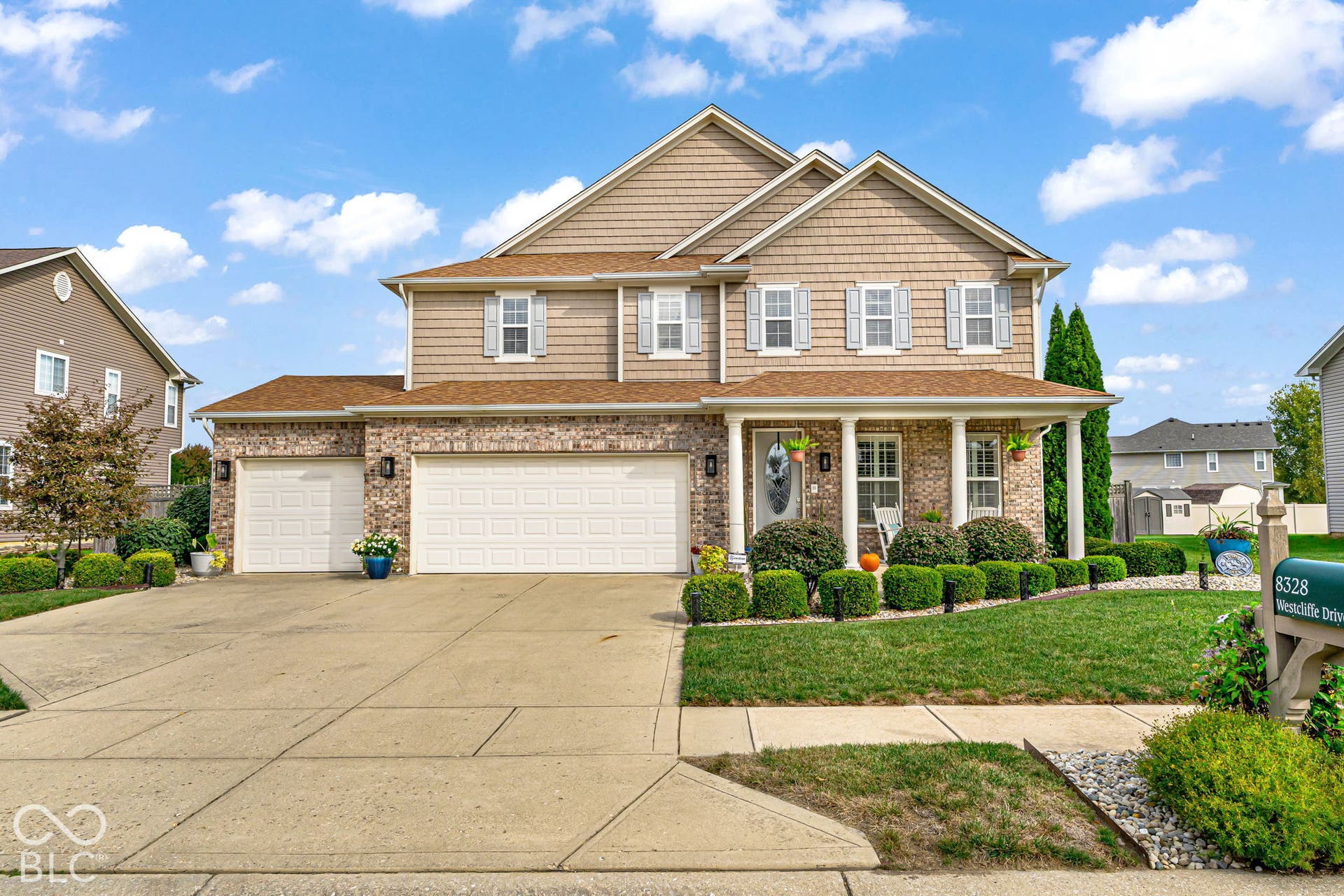 Two-story residence featuring a brick and shake exterior, a covered front porch with columns, a two-car garage, and established front landscaping
