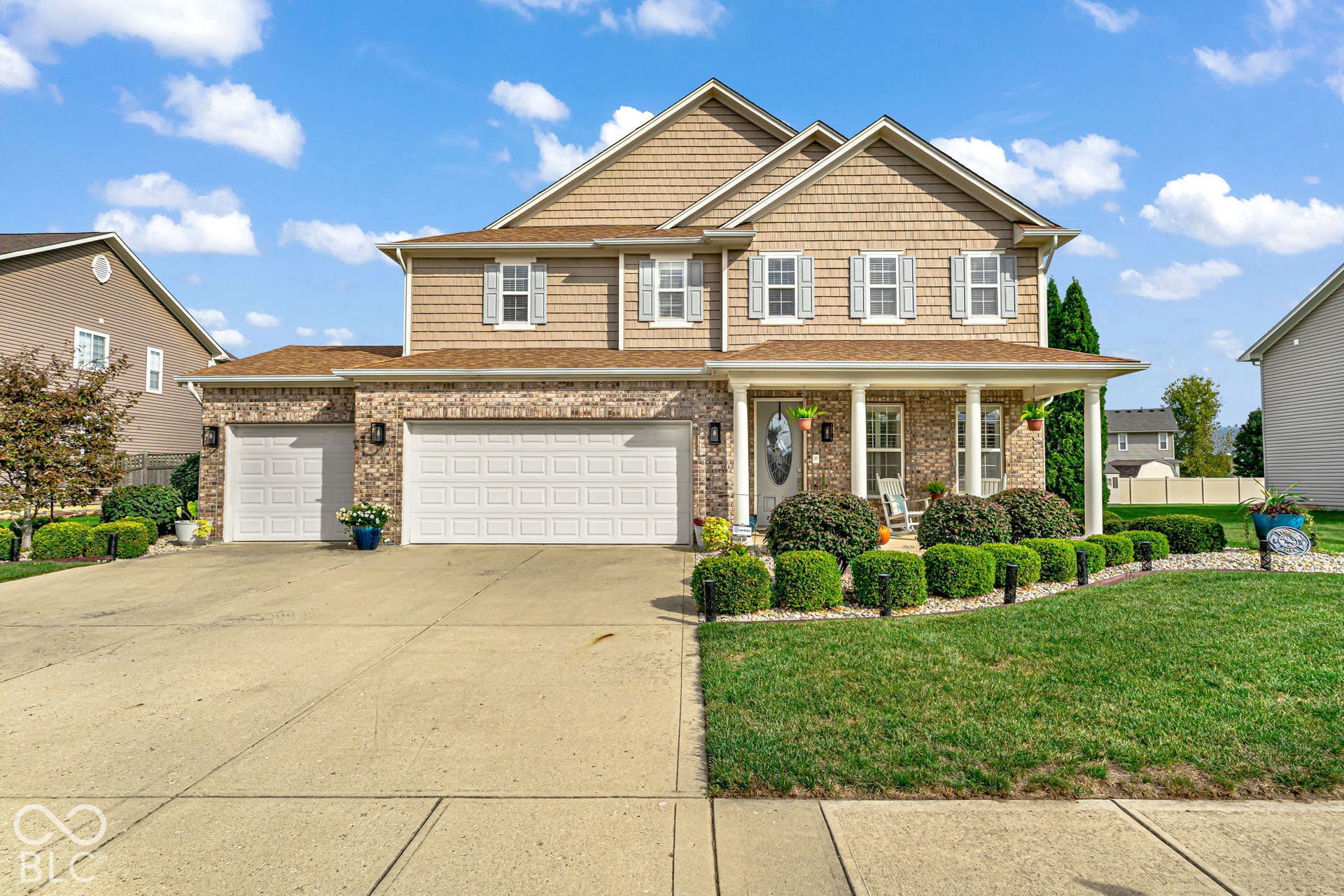 Brick and shingle exterior with a covered front porch, three car garage, and concrete driveway