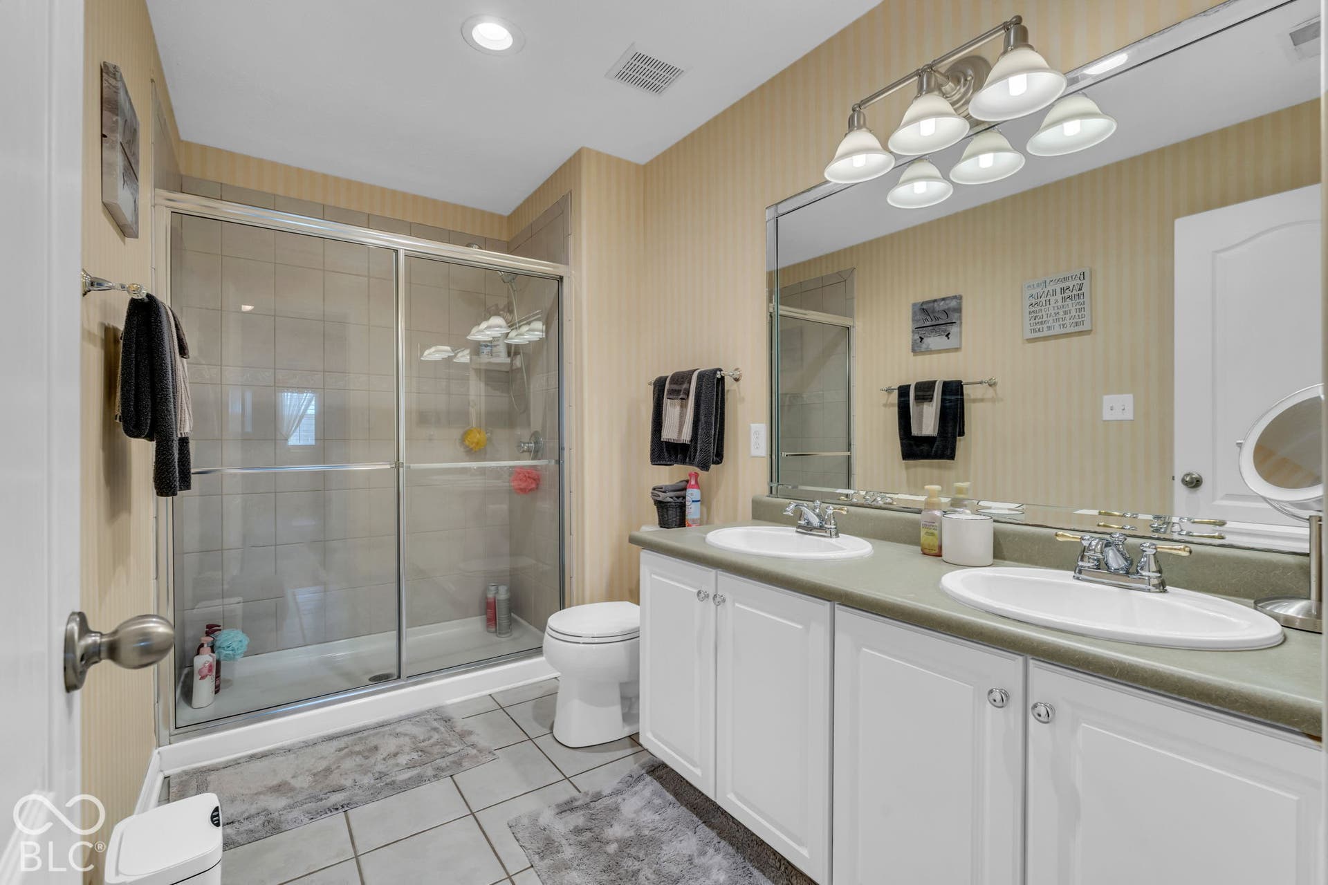 Dual vanity with undermount sinks, full-width mirror, white cabinetry, and a walk-in shower with glass enclosure
