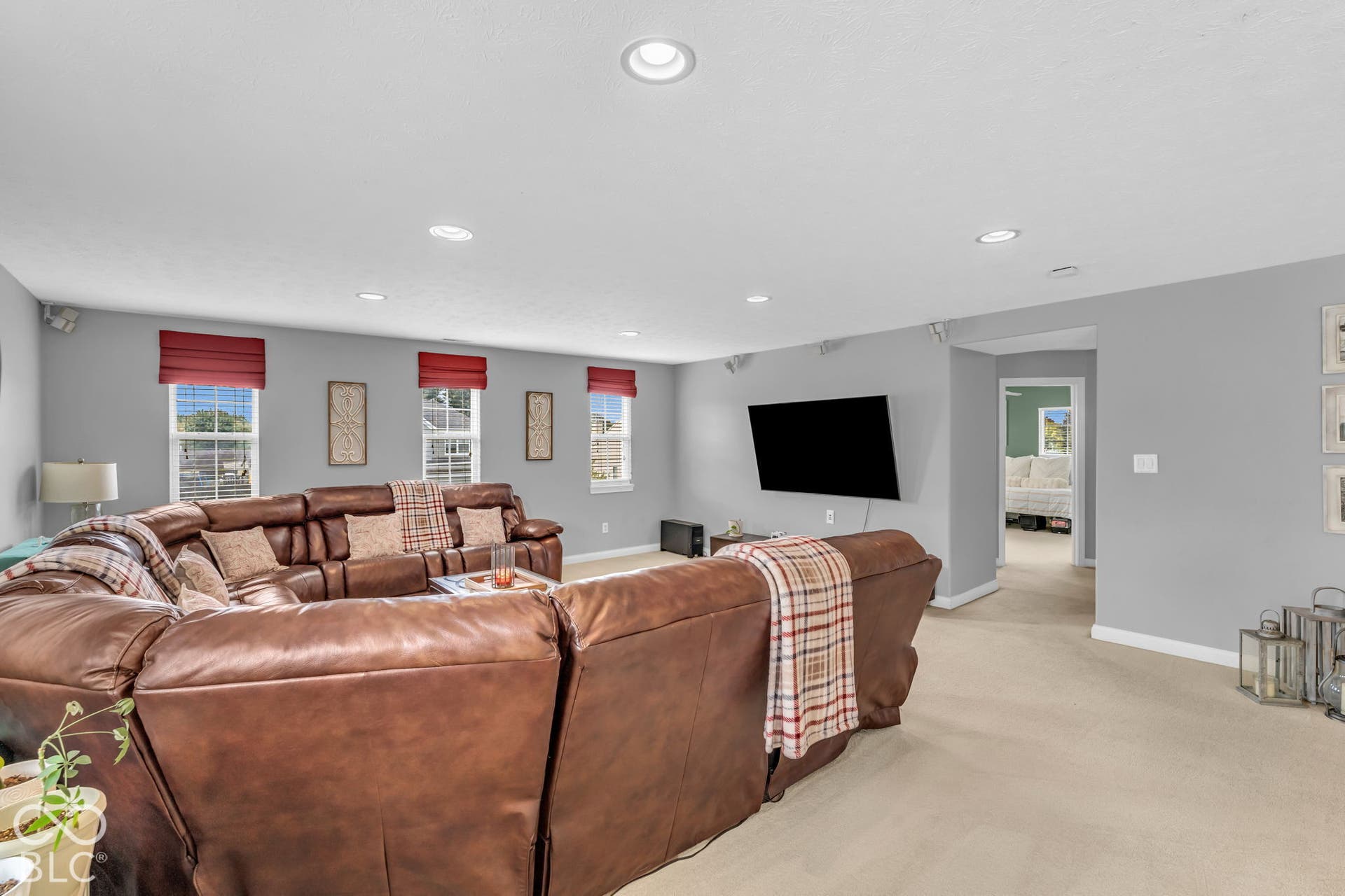 Recessed ceiling lighting, multiple windows with red shades, neutral wall paint, and carpeting throughout