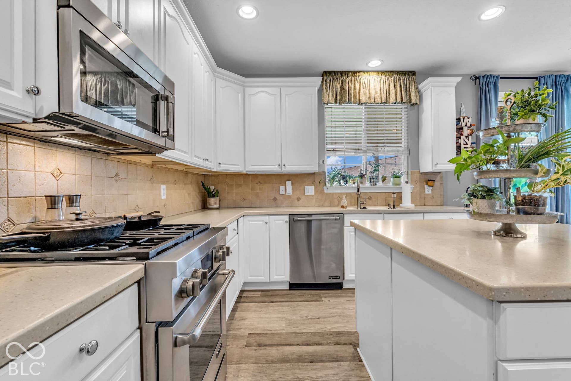 White cabinetry, stainless steel appliances, neutral backsplash, recessed lighting, and wood-finish flooring