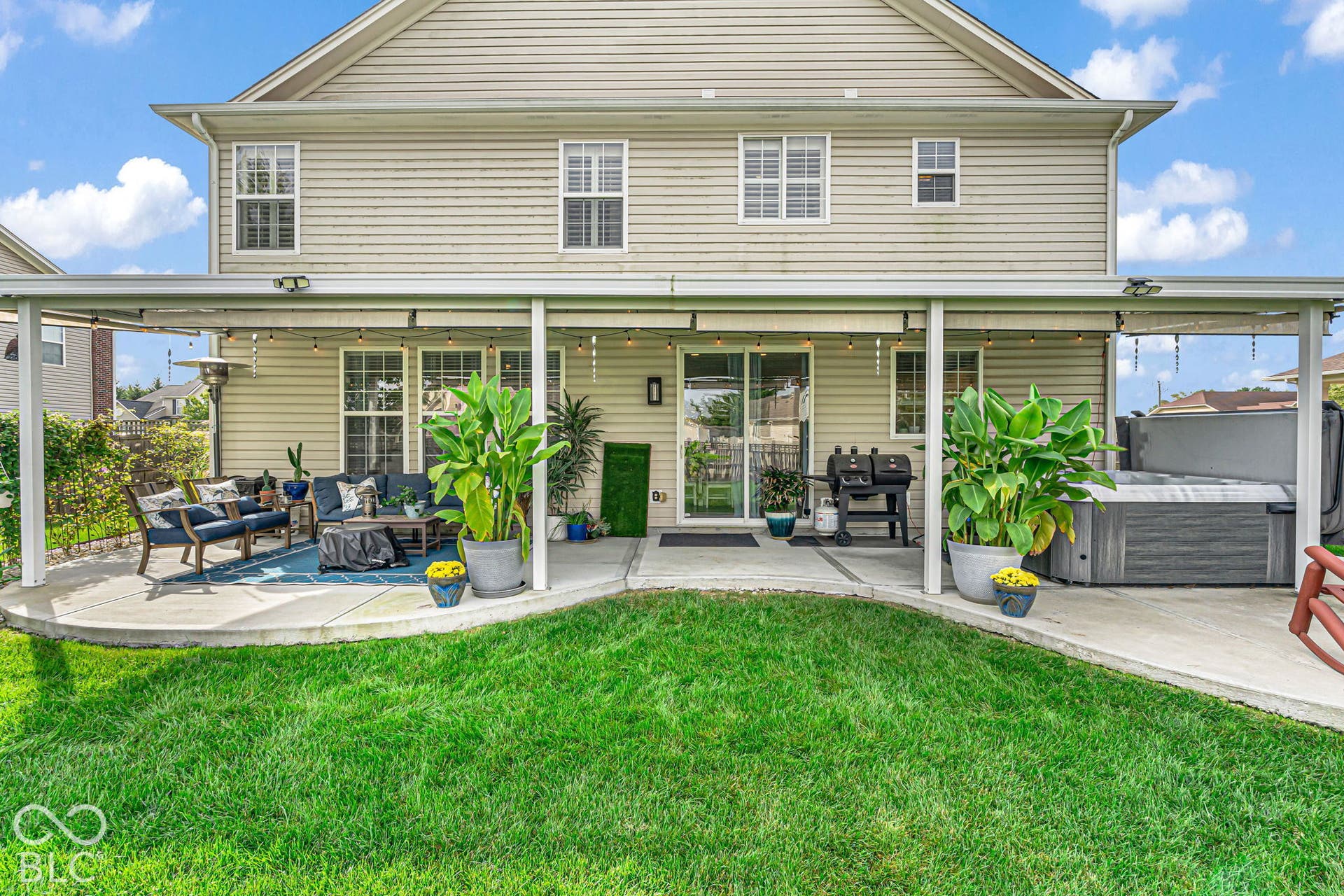 Expansive concrete patio with a full-length covered awning, integrated lighting, and a built-in hot tub