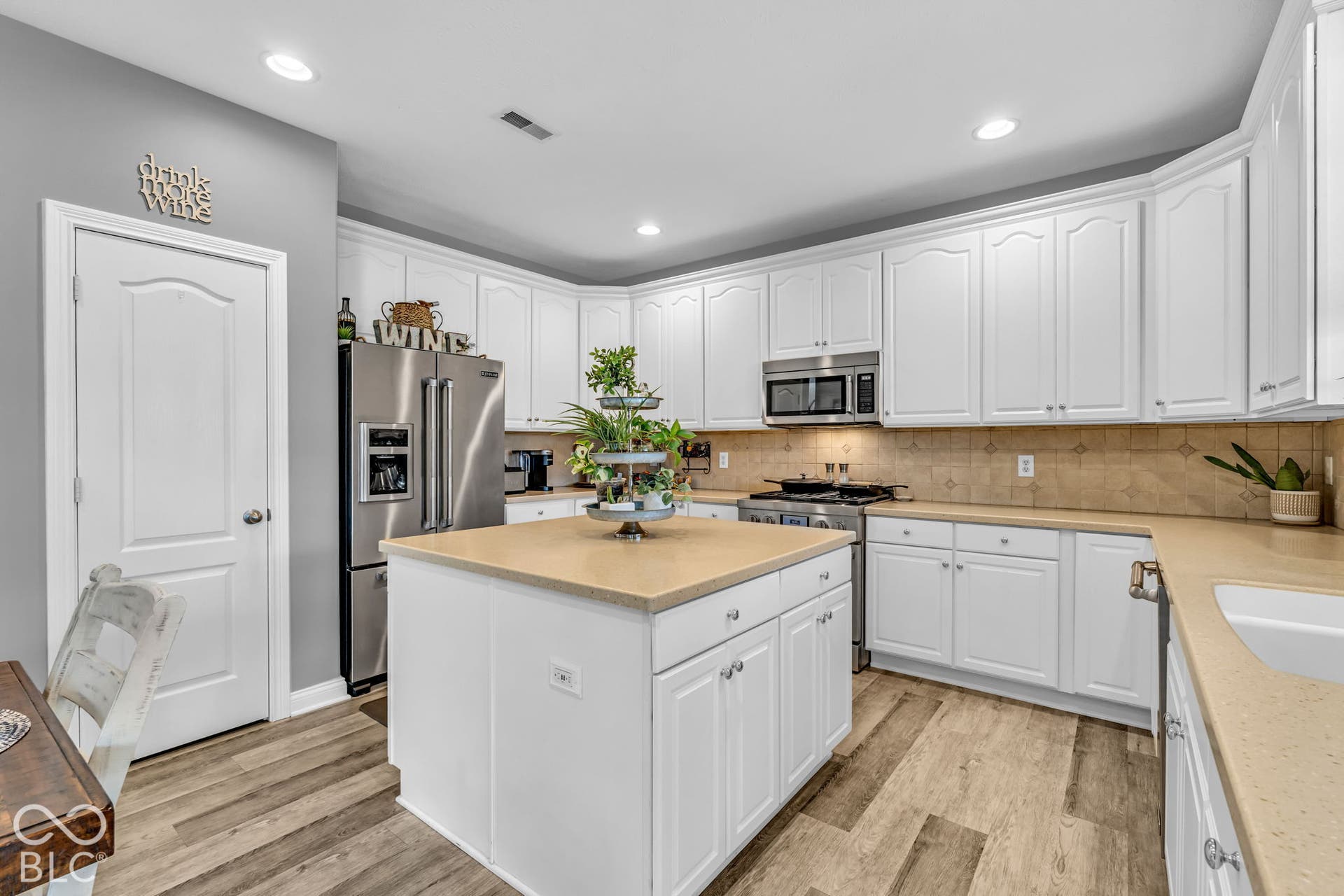 Kitchen featuring white cabinetry, light countertops, stainless steel appliances, wood-finish flooring, and a central island