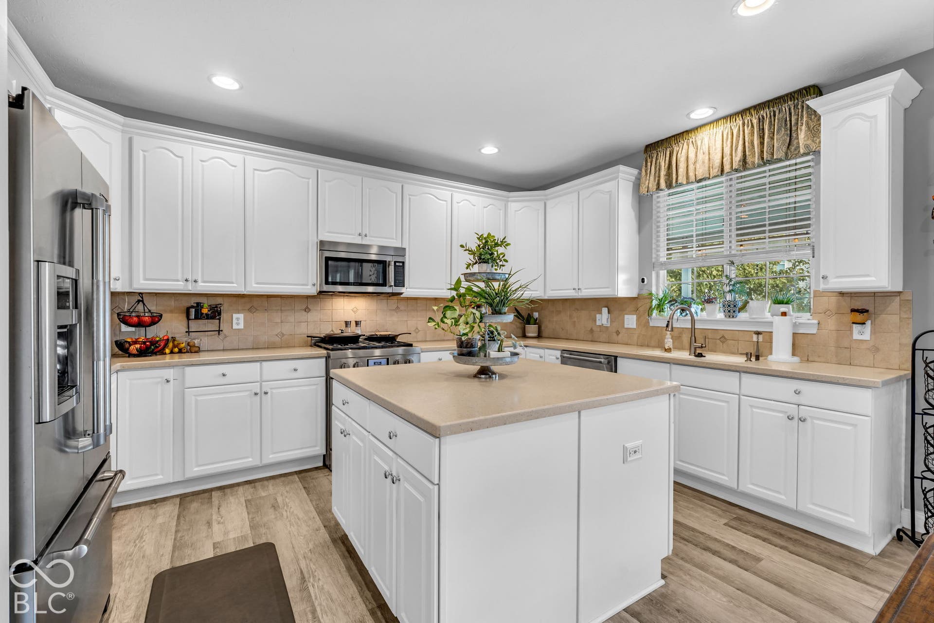 White cabinetry with crown molding, stainless steel appliances, a center island, wood-finish flooring, and a window with blinds