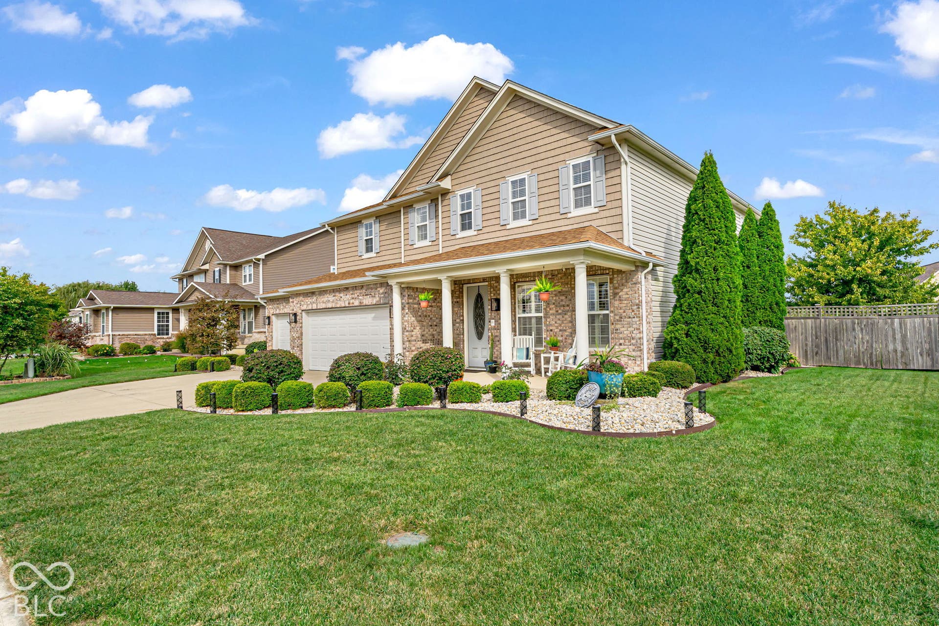 Two-story residence featuring a brick and siding exterior, front porch with columns, a two-car garage, and established landscaping