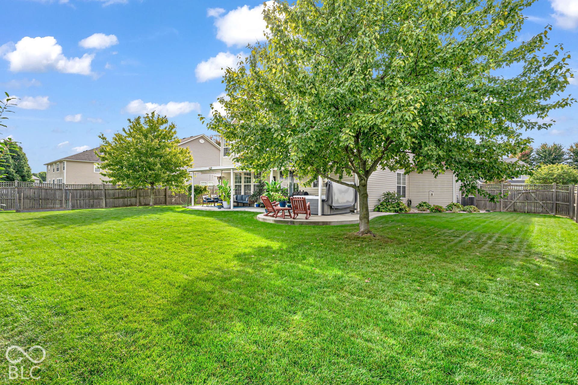 Expansive backyard featuring a lush green lawn, mature trees, a privacy fence, and a patio area with a white pergola