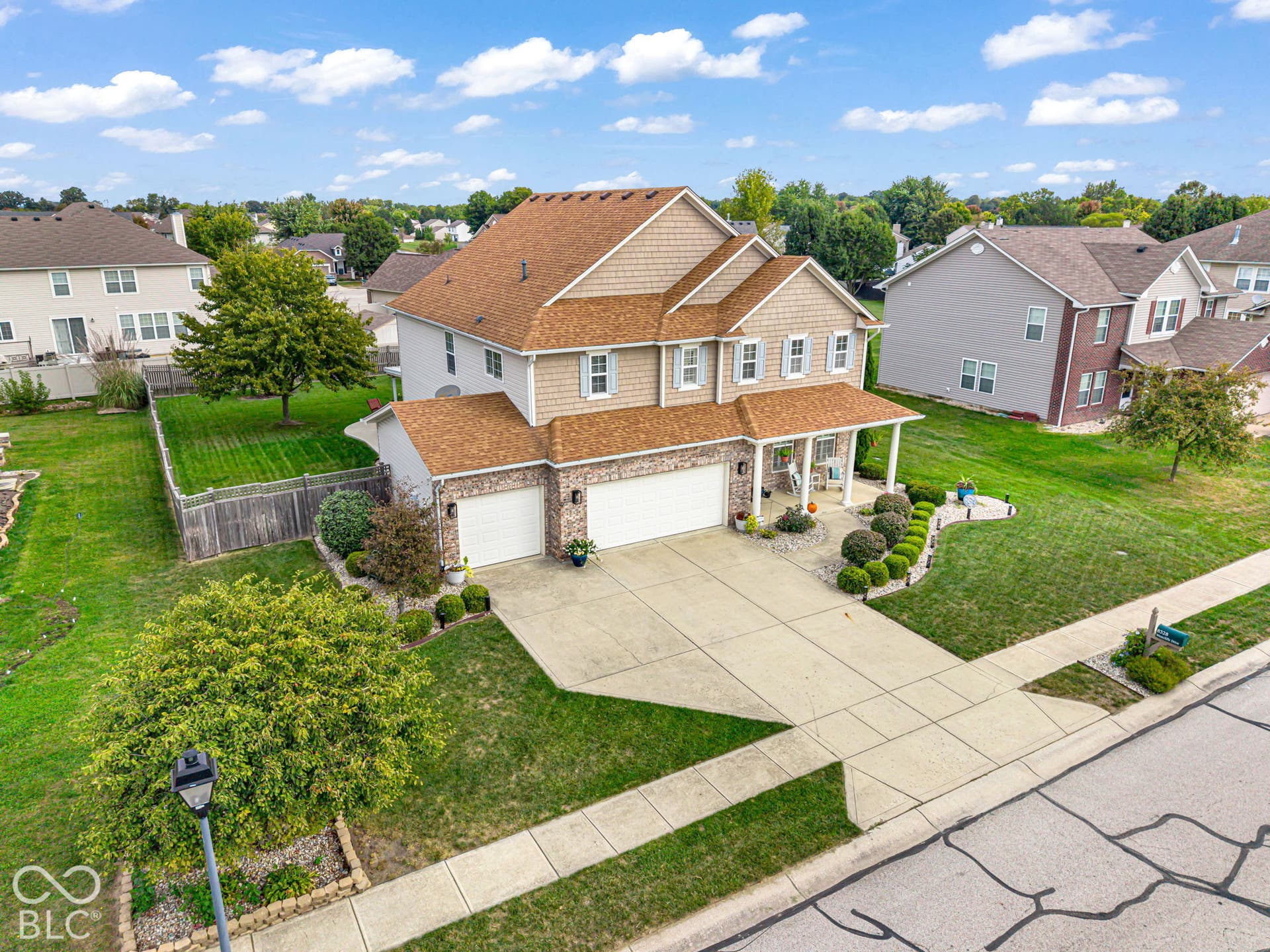 Two-story residence featuring a brick and siding exterior, multi-car garage, covered front porch, concrete driveway, and established landscaping