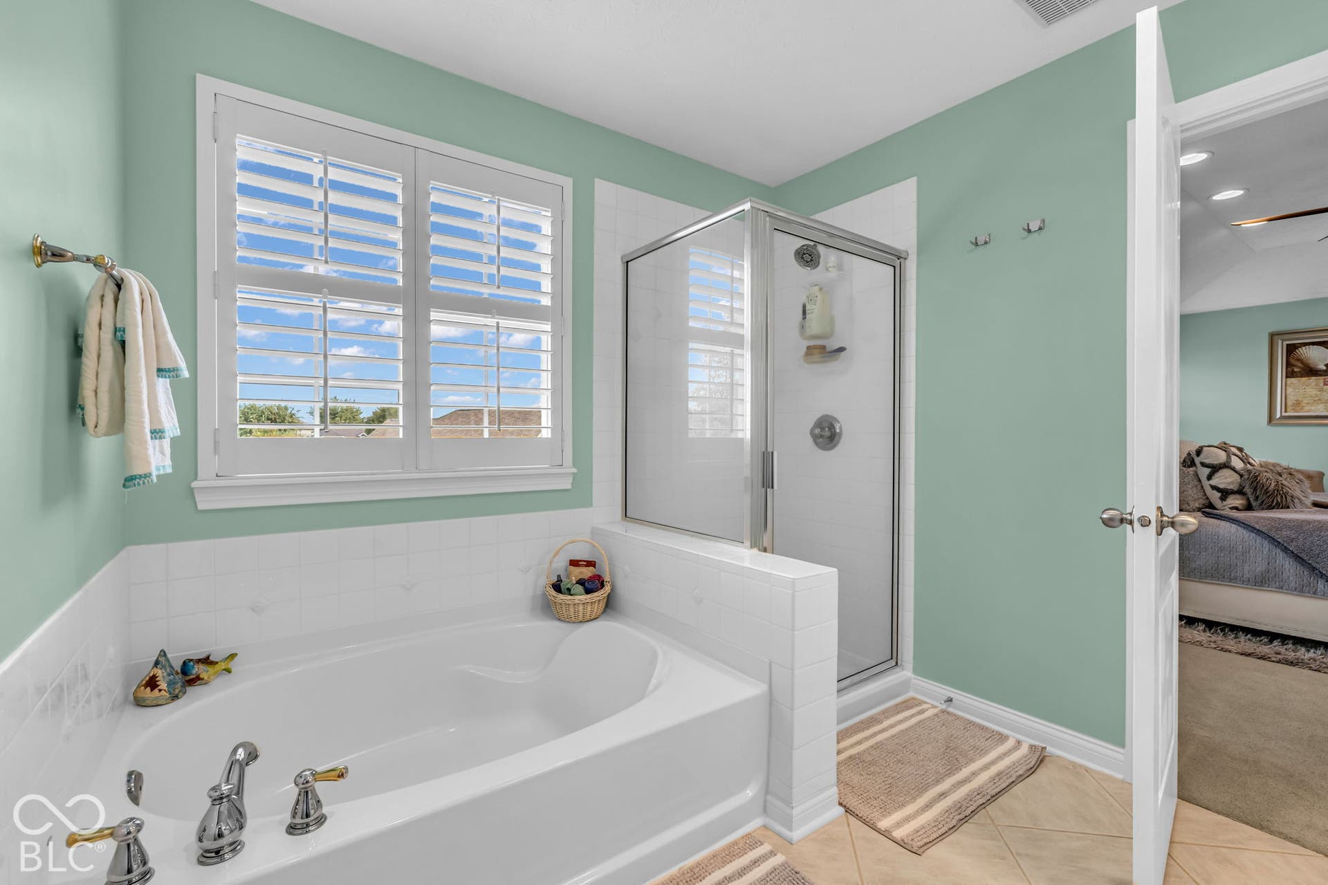 Recessed soaking tub with polished chrome fixtures, white tile surround, and a double window featuring white plantation shutters