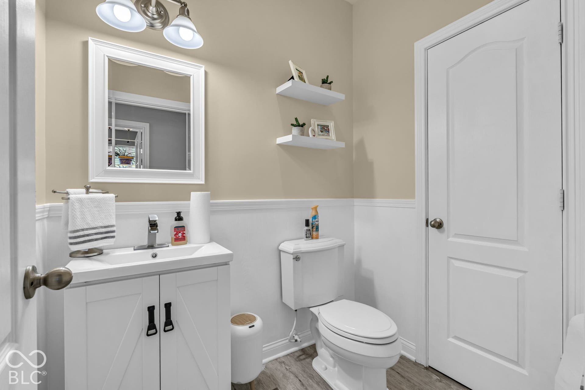 White vanity with modern black hardware, wood-finish flooring, white paneled lower walls, and neutral-toned upper walls