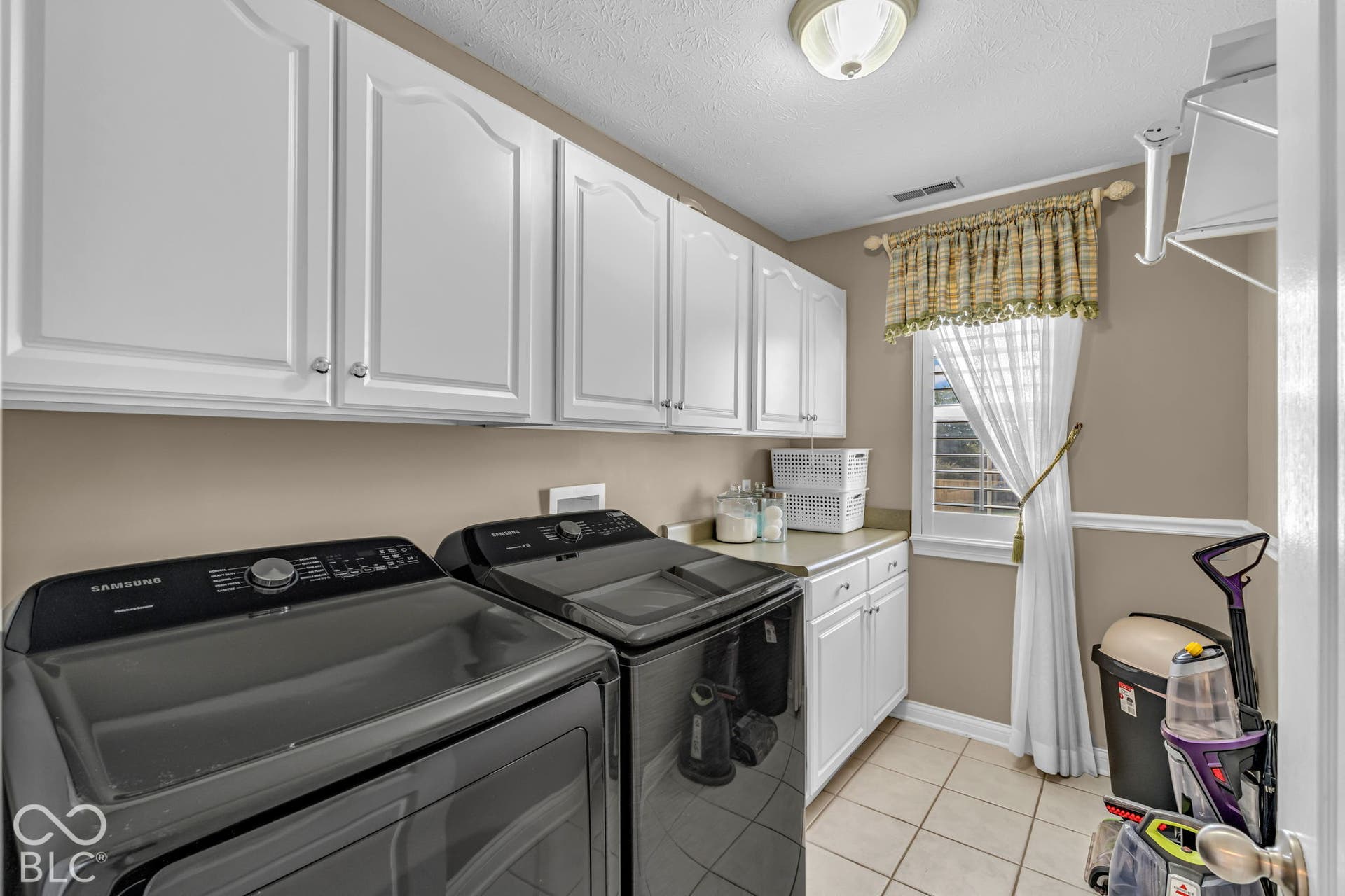 White shaker-style cabinetry, light-toned countertop space, window with natural light, and tile flooring