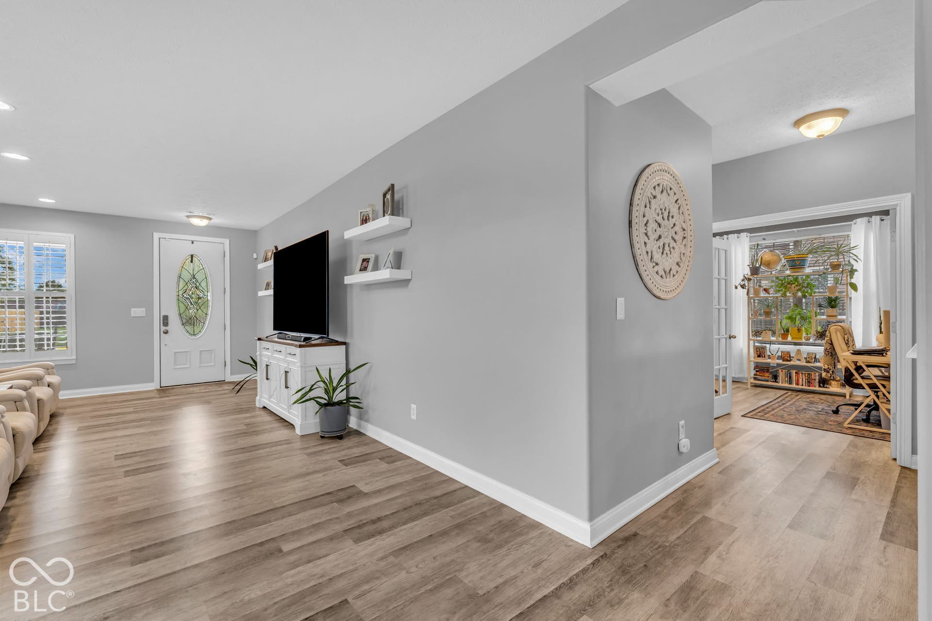 Wood-finish flooring throughout, white entryway door with decorative glass inlay, recessed ceiling lighting, and French doors