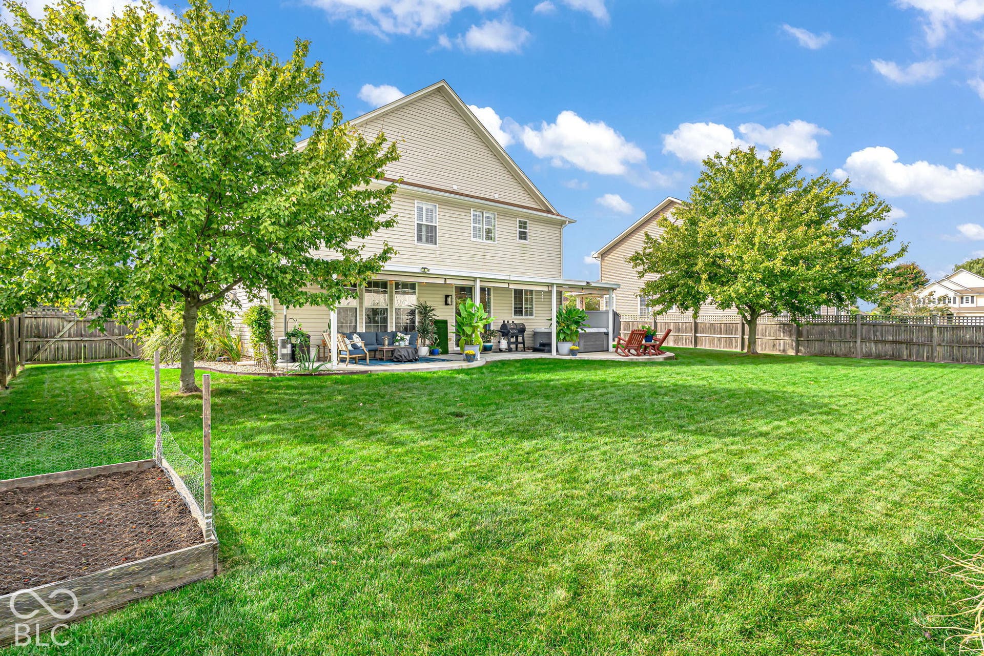Expansive backyard featuring a manicured lawn, established trees, privacy fencing, and a covered patio