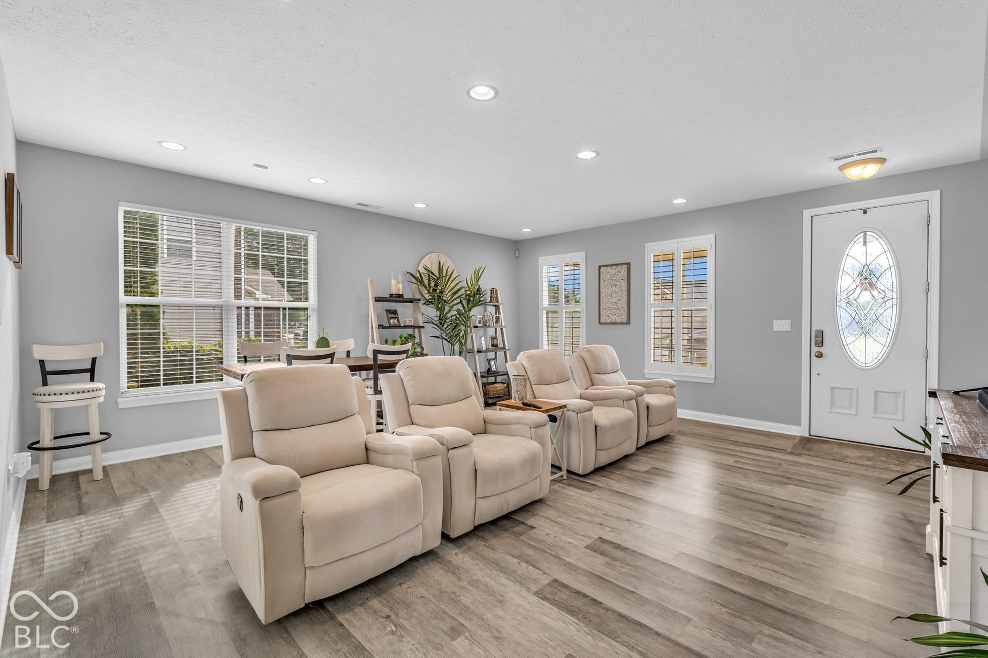 Wood-finish flooring, recessed lighting, multiple windows with blinds, and a white entry door with decorative glass inlay