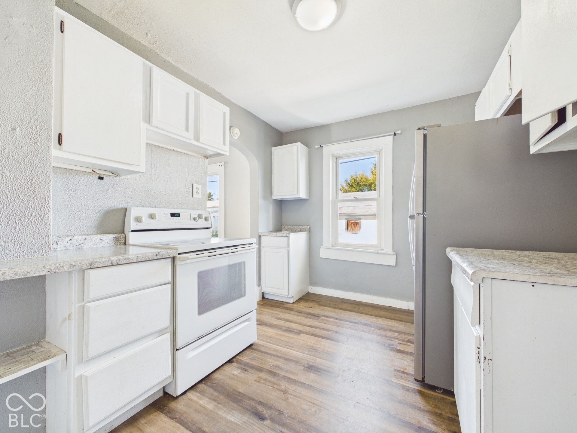 Kitchen featuring wood-finish flooring, white cabinetry, a white electric range, and a stainless steel refrigerator