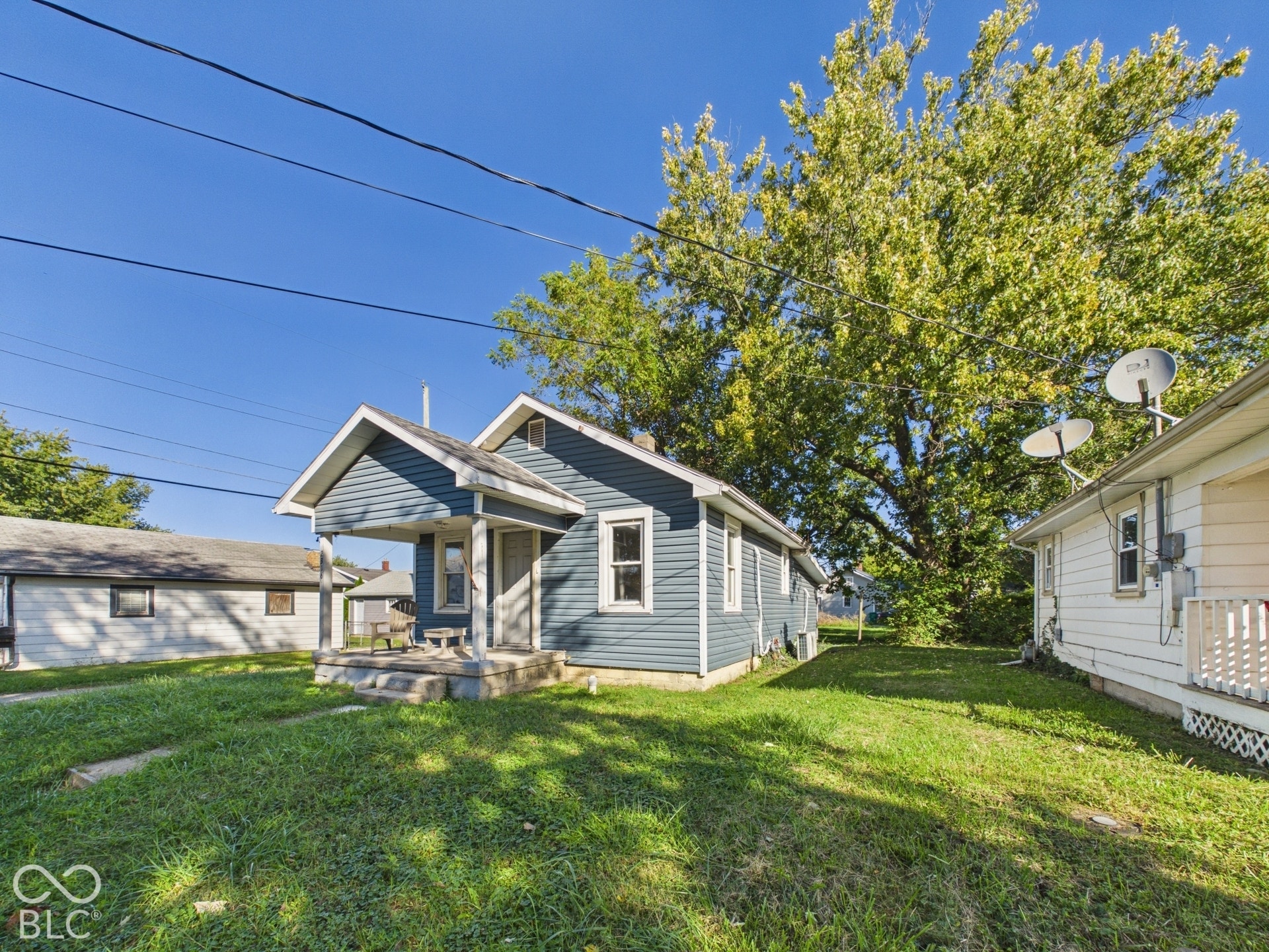Charming cottage with board-and-batten siding and front porch entry, situated on a spacious lawn with mature shade trees