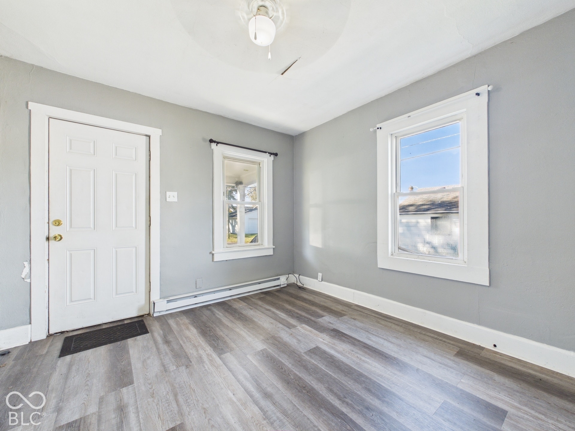 Wood-finish flooring with a neutral gray tone, white trim and baseboards, and a white paneled door