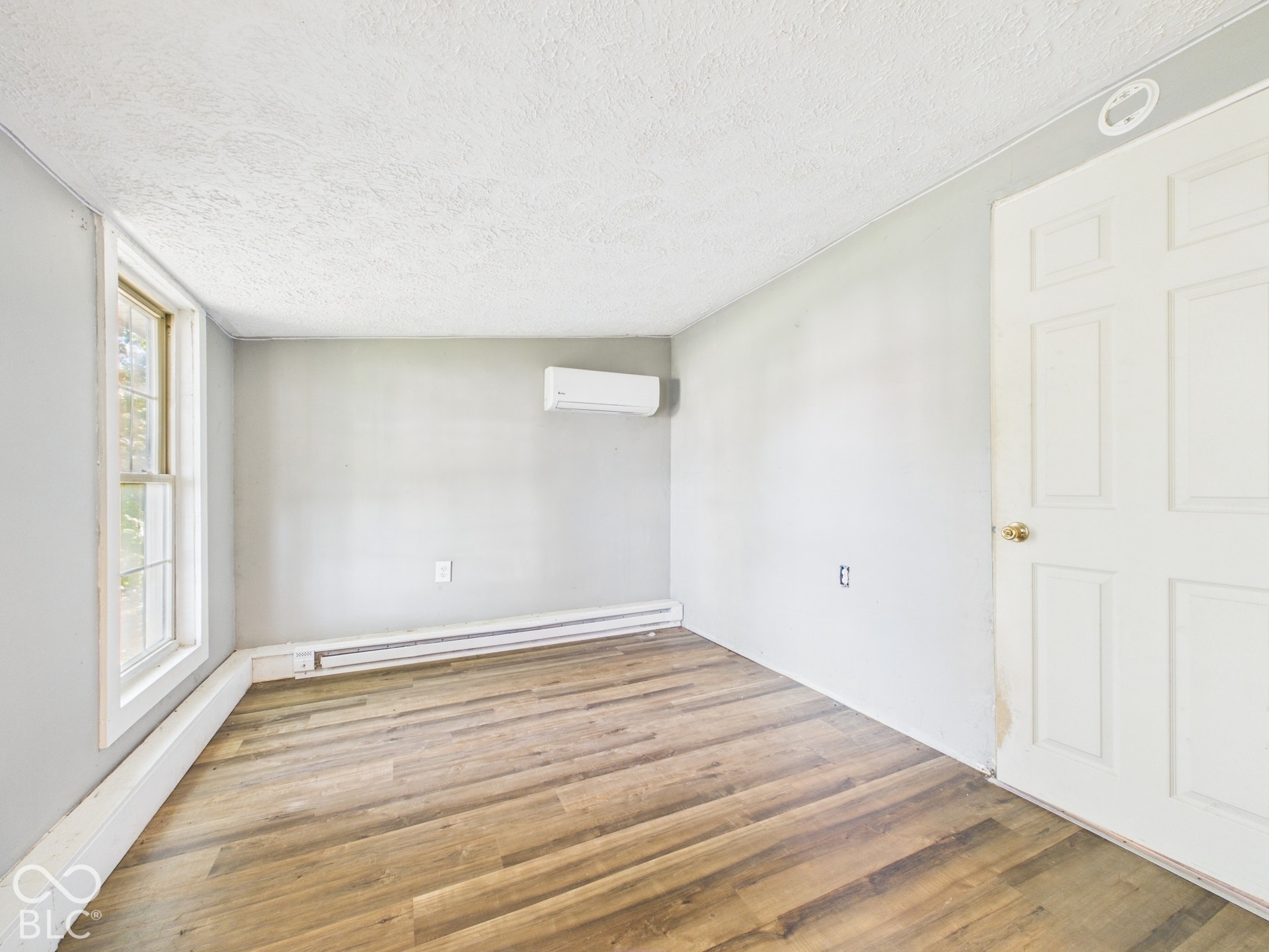 Wood-finish flooring, light gray wall paint, and a wall-mounted climate control unit
