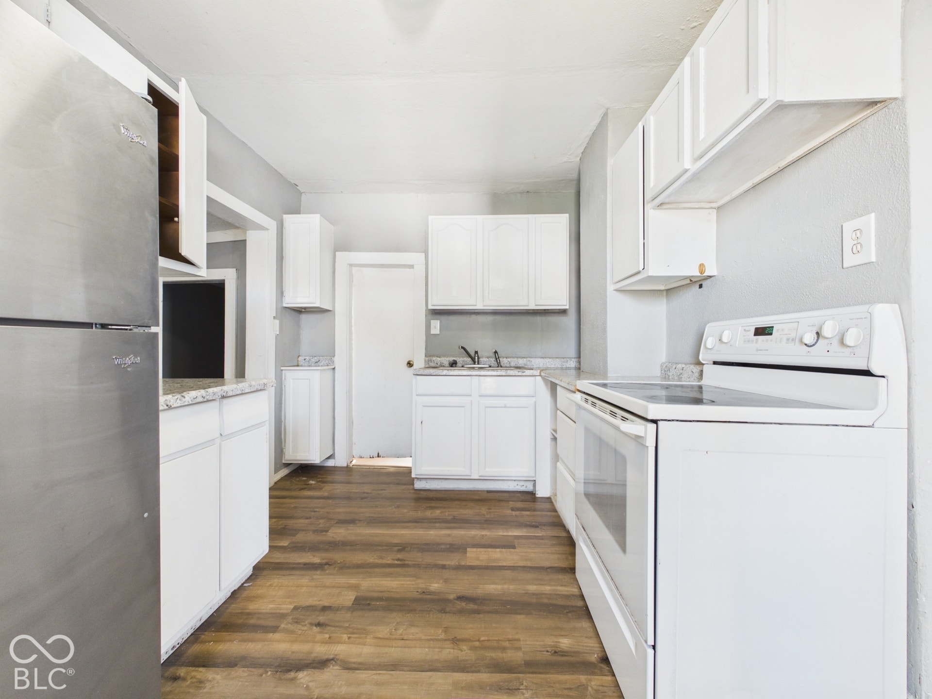 Kitchen featuring wood-finish flooring, white cabinetry, a stainless steel refrigerator, white electric range, and light-colored countertops