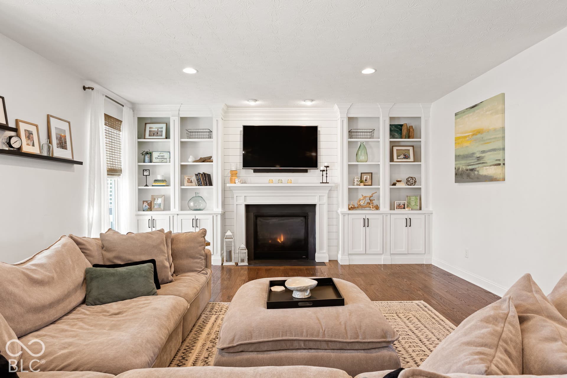 Fireplace with a white mantel, flanked by built-in shelving and cabinetry, recessed ceiling lighting, and wood-finish flooring