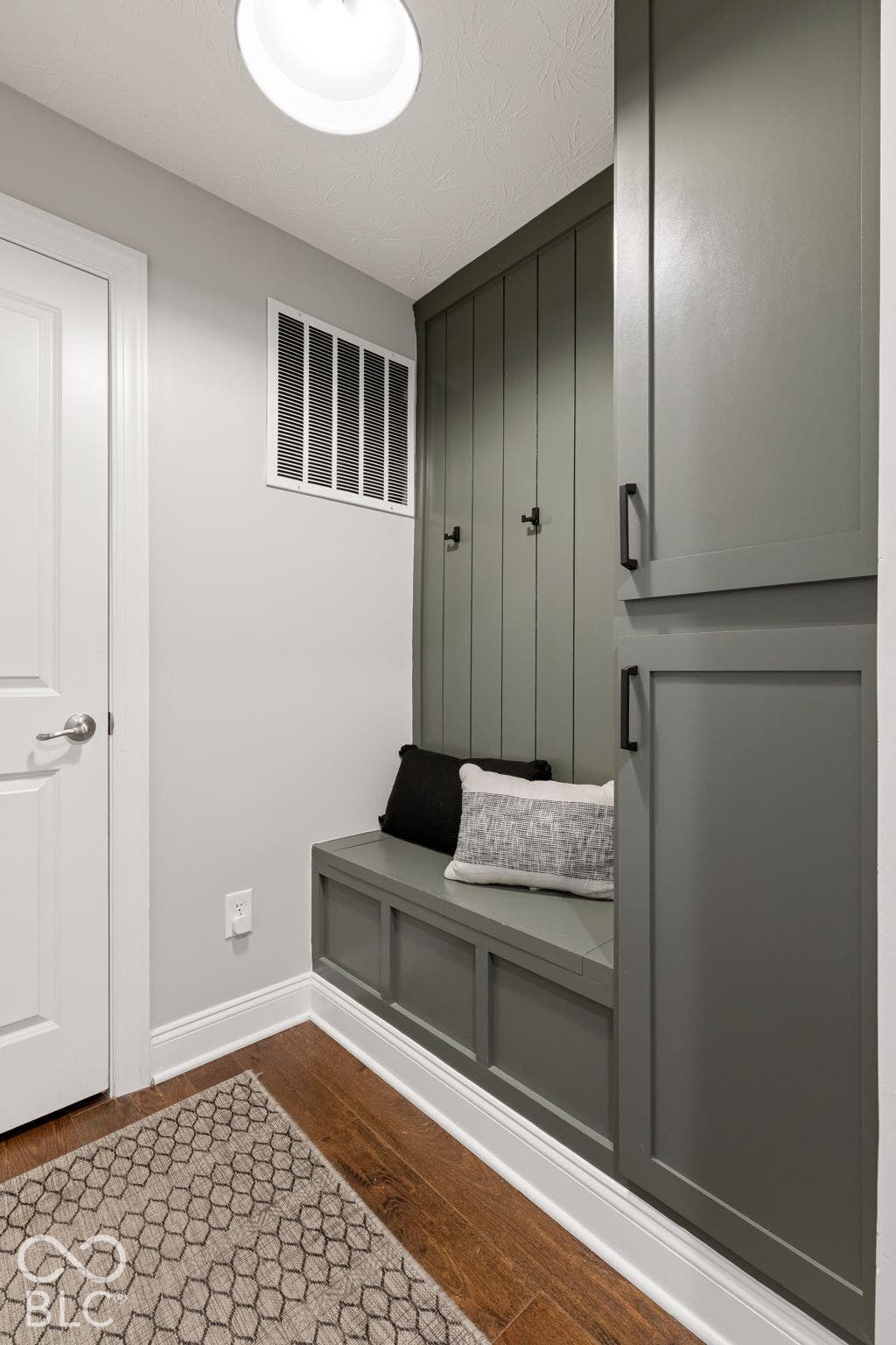 Built-in bench seating with vertical paneling, integrated storage cabinetry, dark wood-finish flooring, and a flush-mount overhead light fixture