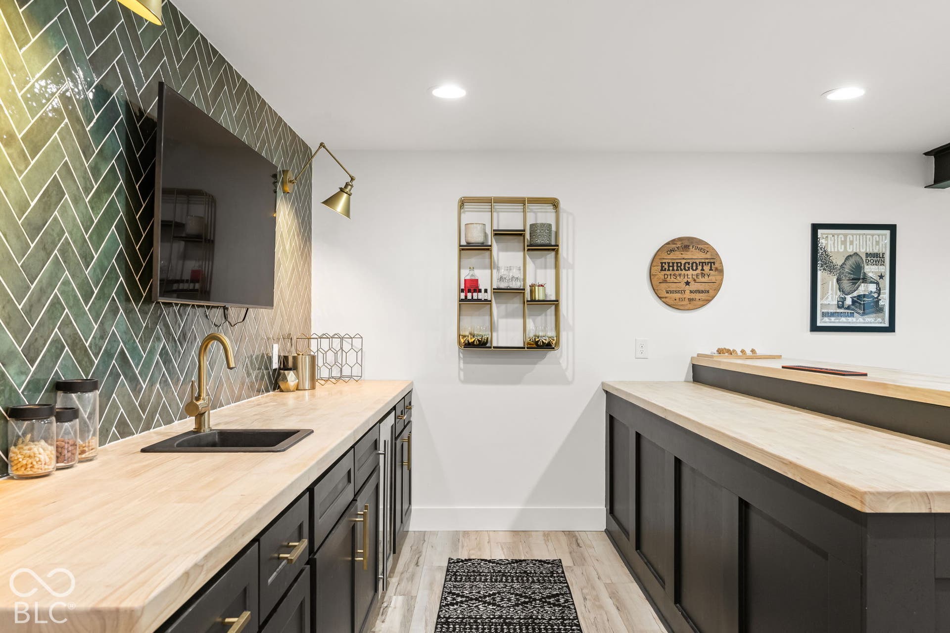 Herringbone tile wall, integrated beverage refrigerator, wood-finish countertops, recessed lighting, and a built-in bar