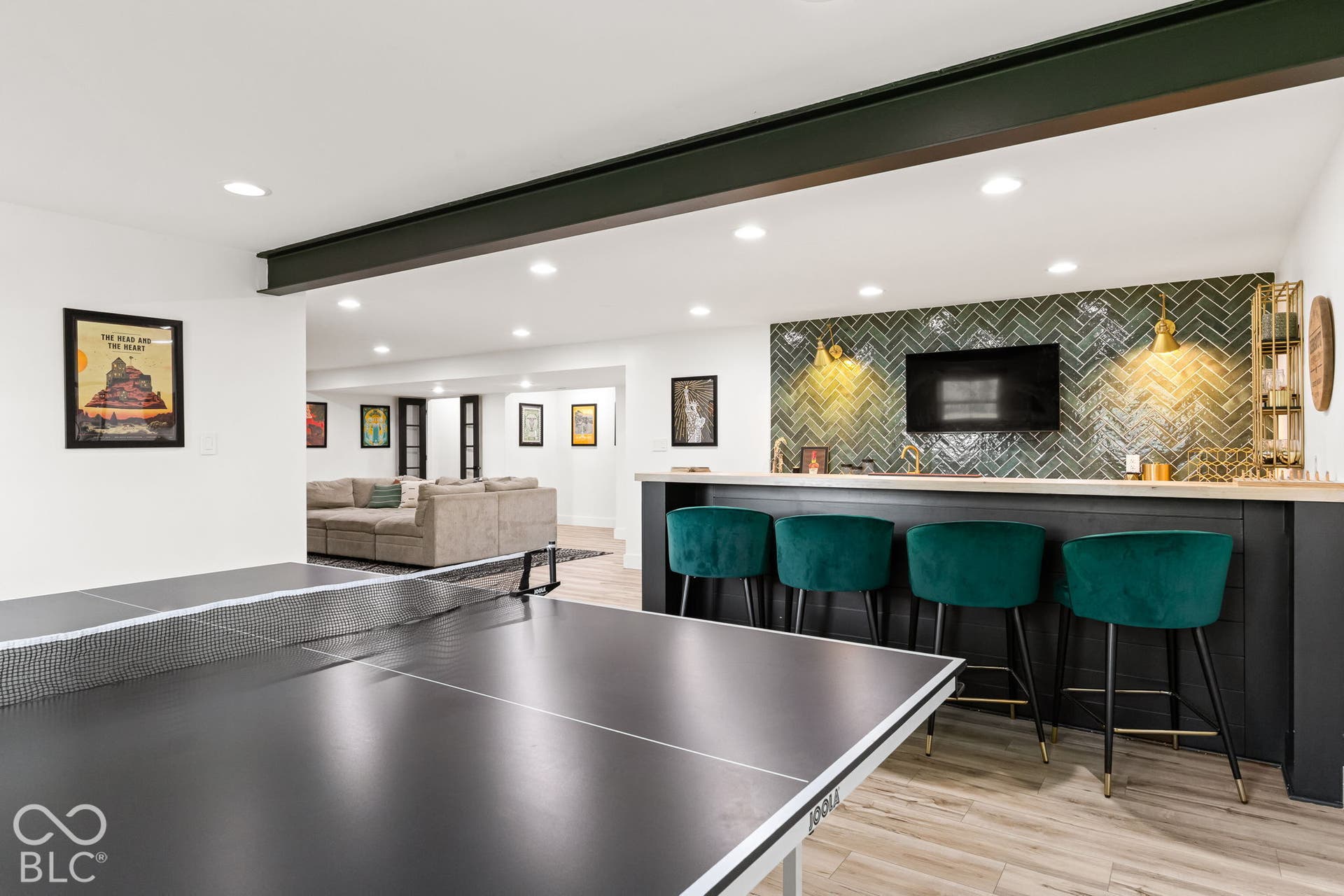 Recessed lighting, wood-finish flooring, accent wall with herringbone tile, built-in bar with wood countertop, and exposed structural beam