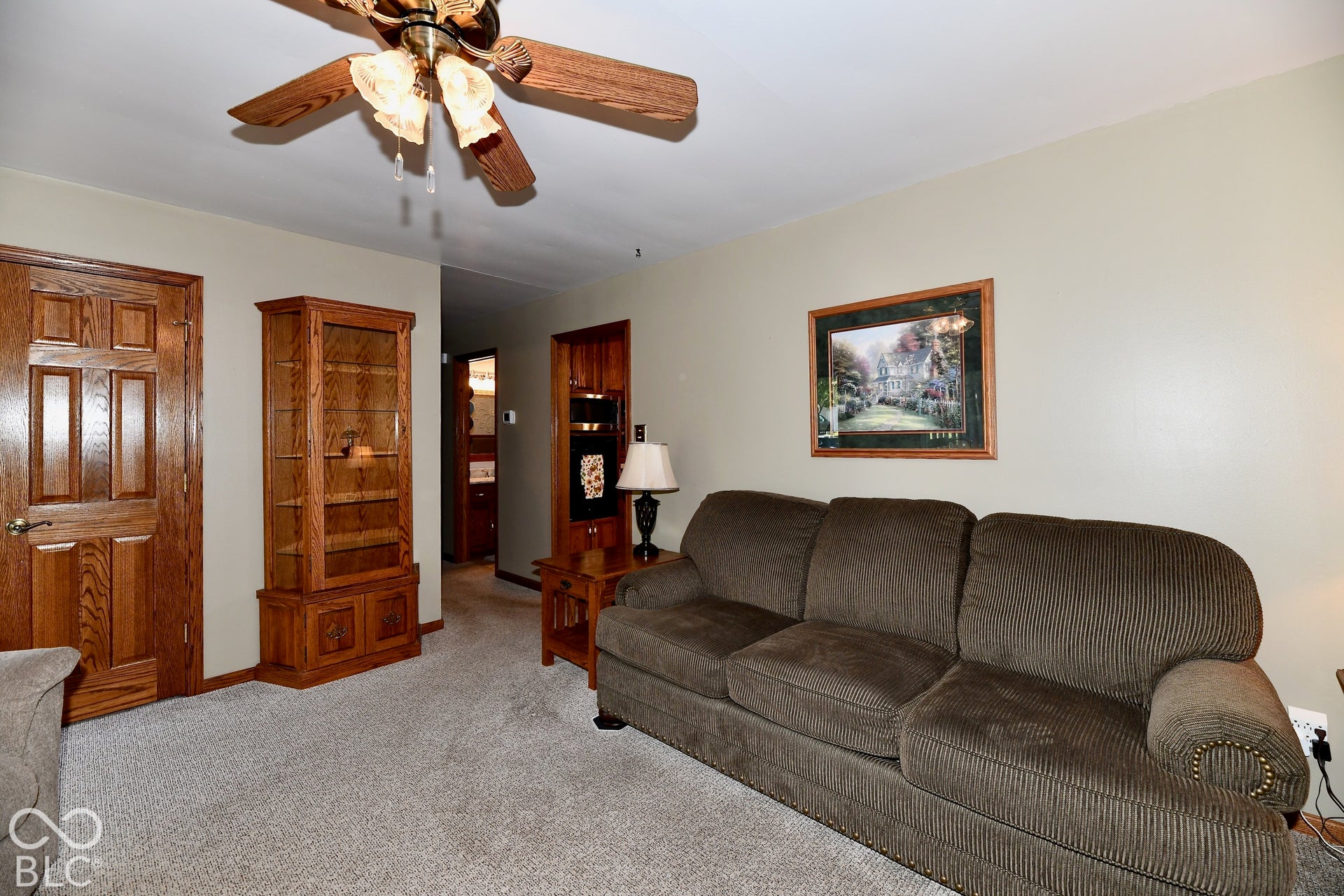 Spacious living room featuring a wood-finish ceiling fan with integrated lighting and neutral carpeting