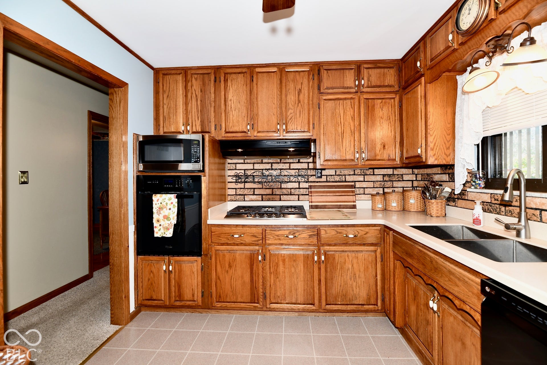Kitchen featuring wood cabinetry, solid surface countertops, a brick-style backsplash, a deep dual basin sink with a gooseneck faucet, and integrated appliances