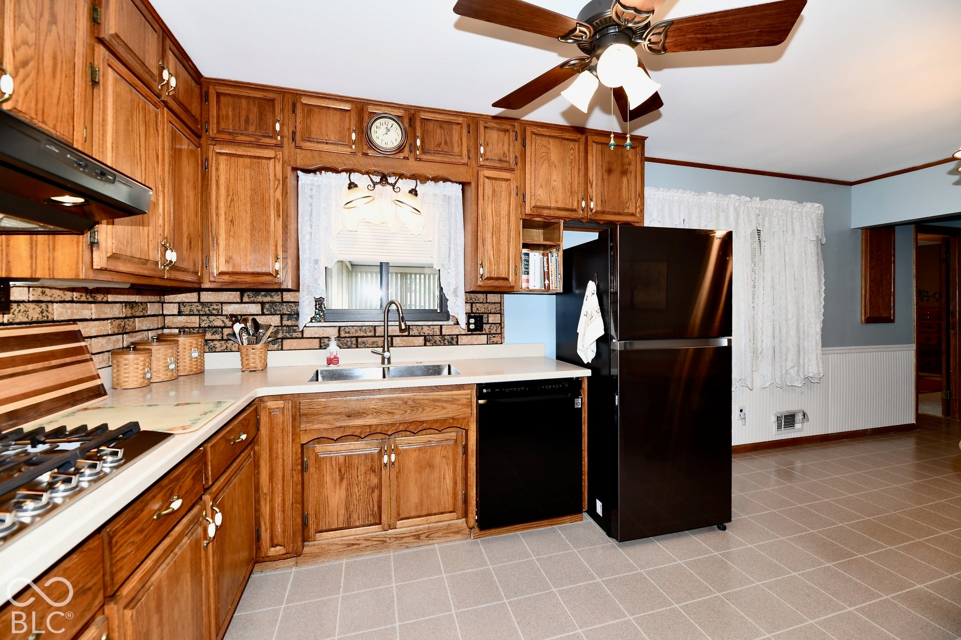 Wood-finish cabinetry, vinyl flooring, brick-patterned backsplash, and a ceiling fan with integrated lighting