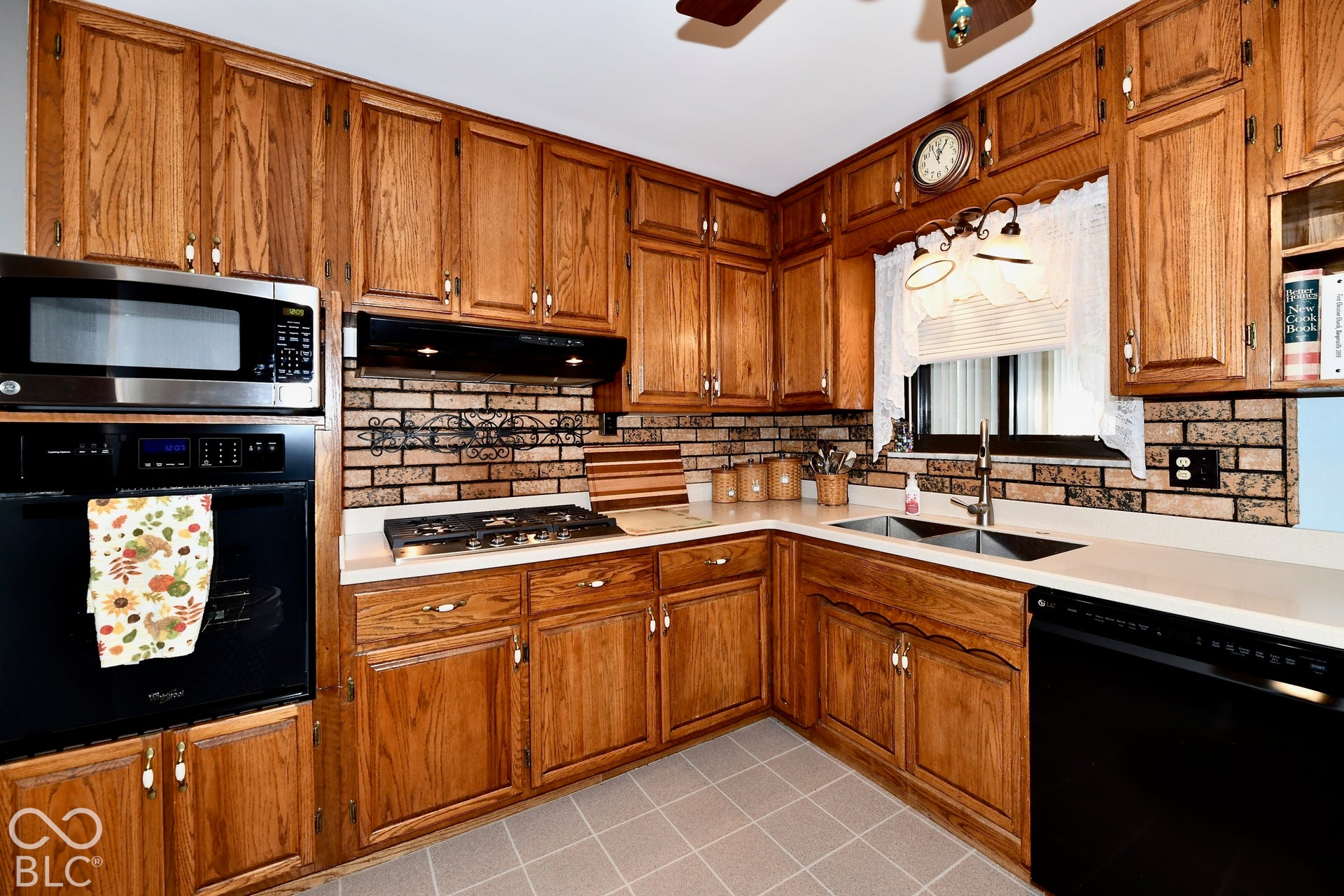 Warm oak cabinetry with brushed nickel hardware frames this kitchen, featuring stainless steel appliances, a five-burner gas cooktop, faux brick backsplash, and solid surface countertops