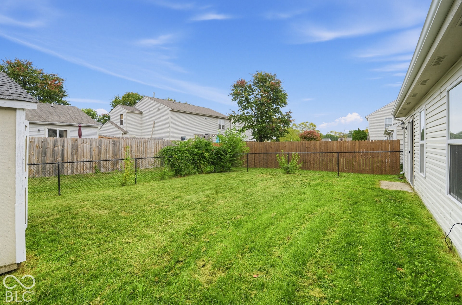 Rear yard featuring a grass lawn, wood privacy fencing, chain-link perimeter fencing, and a detached storage structure