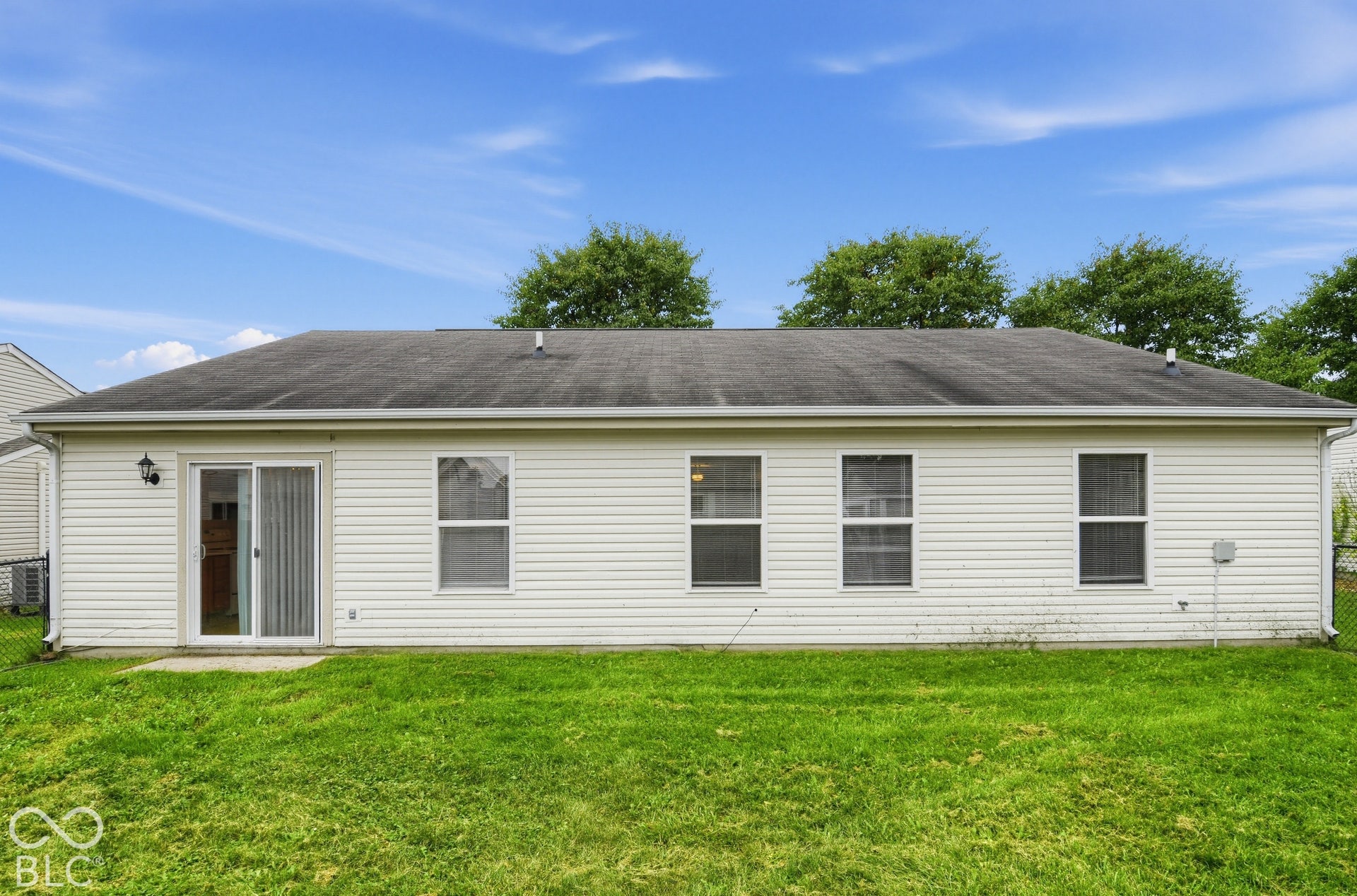 Horizontal vinyl siding exterior featuring a multi-paneled sliding glass door, four rectangular windows, and a paved concrete patio slab