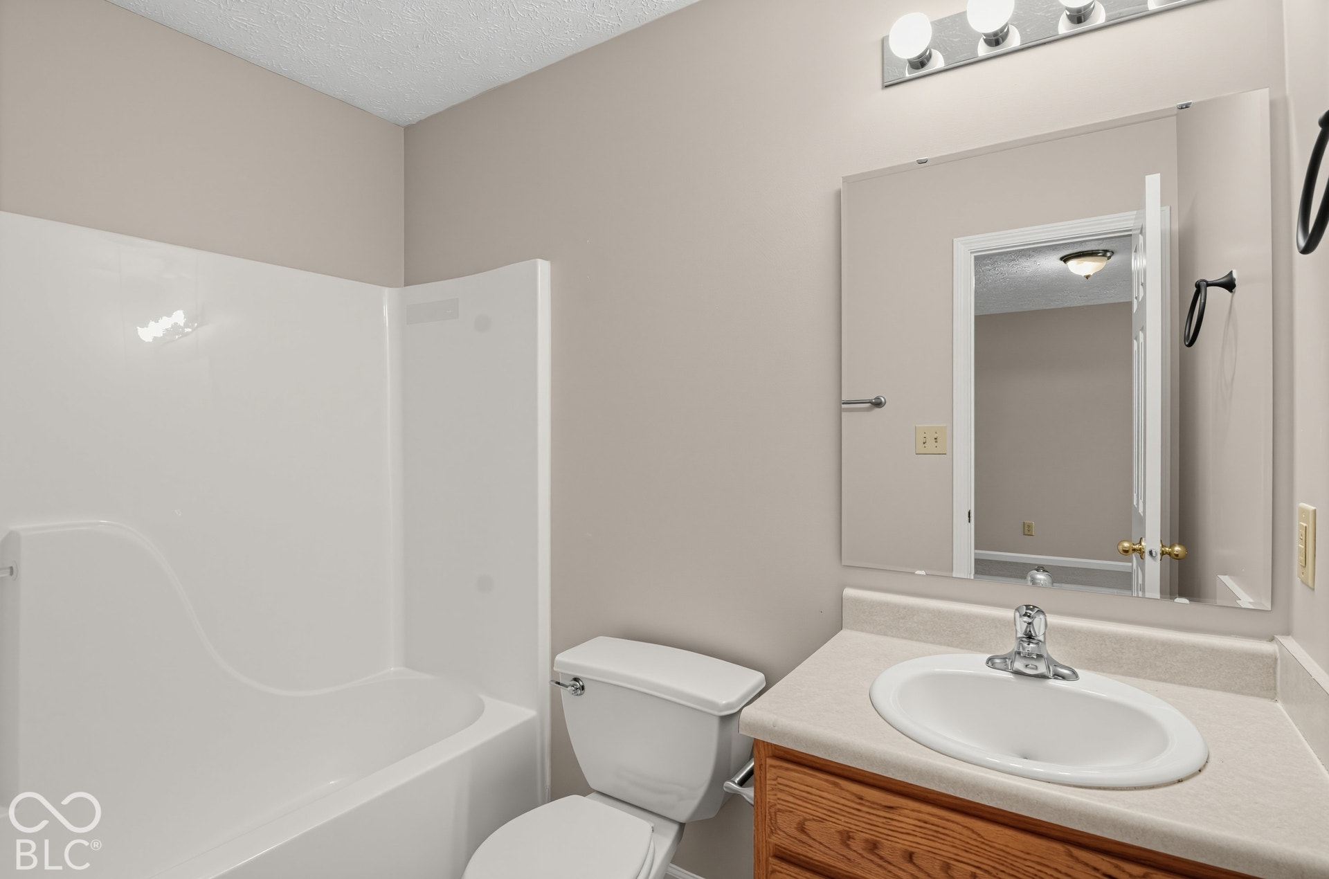 Bathroom featuring a composite tub and shower surround, wood-finish vanity with a neutral countertop, integrated oval sink, and a multi-bulb light fixture