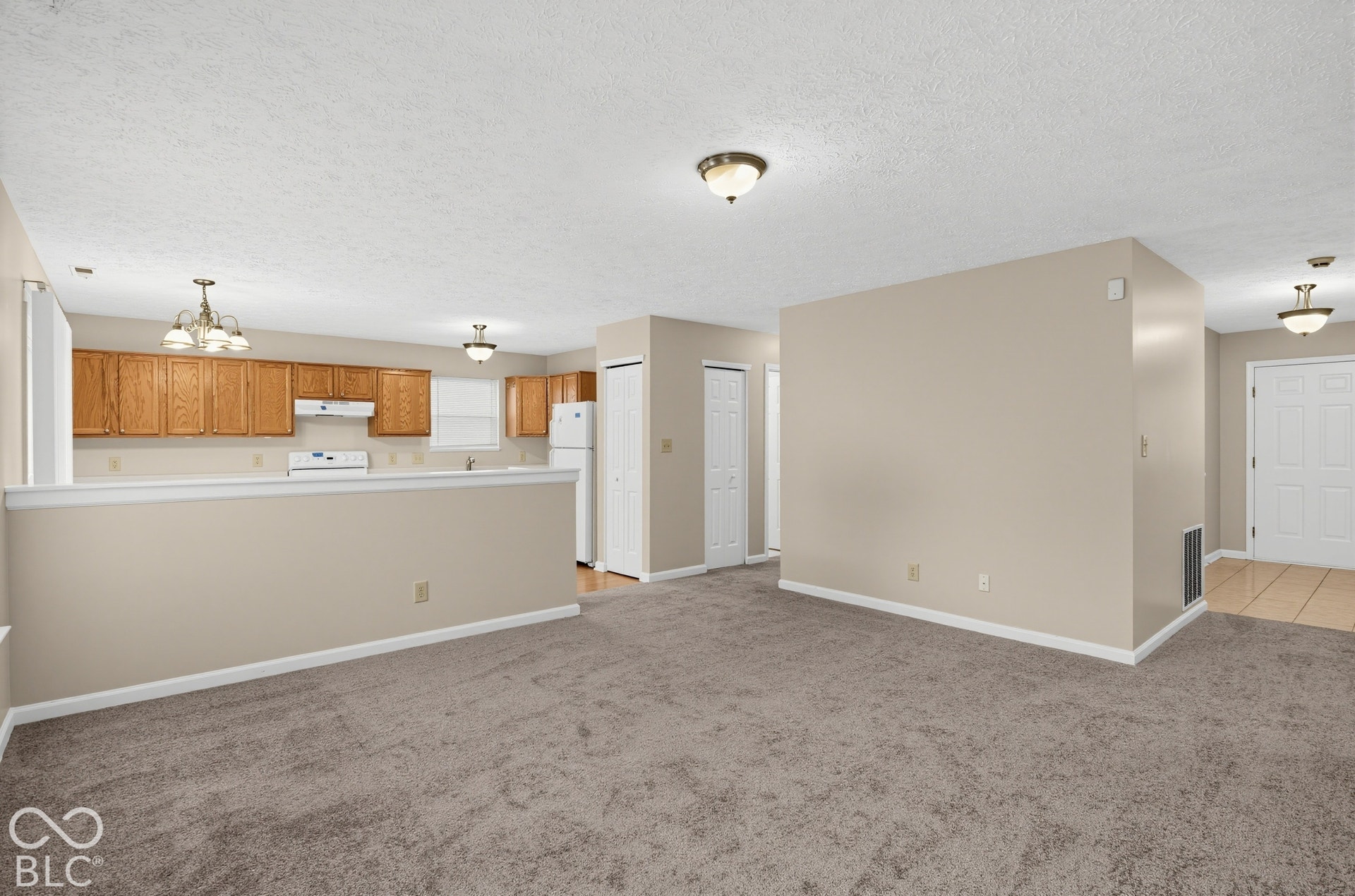 Open-concept interior featuring wood cabinetry, wall-to-wall carpeting, tile flooring, and multiple ceiling-mounted light fixtures