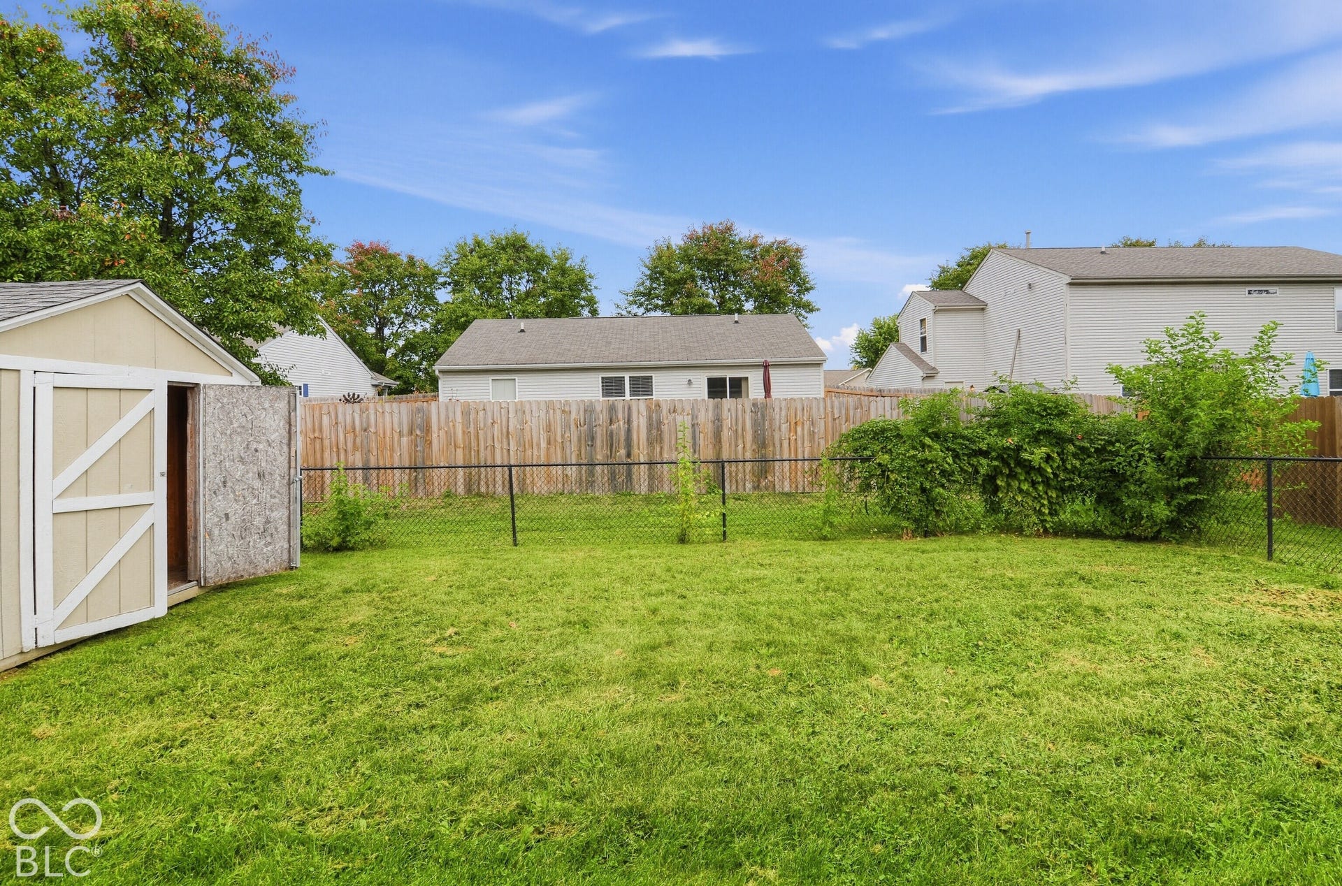 Backyard featuring a grass lawn, wooden perimeter fencing, chain-link enclosure, and detached storage shed