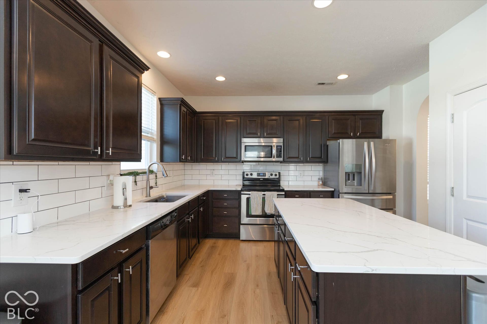 Kitchen featuring dark wood cabinetry, white quartz countertops, subway tile backsplash, stainless steel appliances, and wood-finish flooring