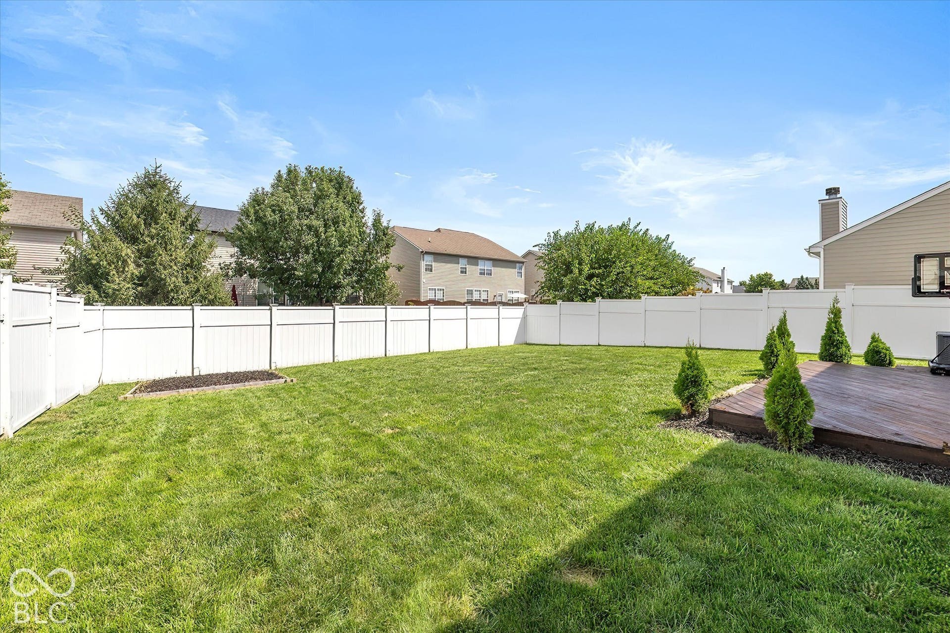 Expansive backyard featuring a manicured lawn, white privacy fencing, and a wood-finish deck