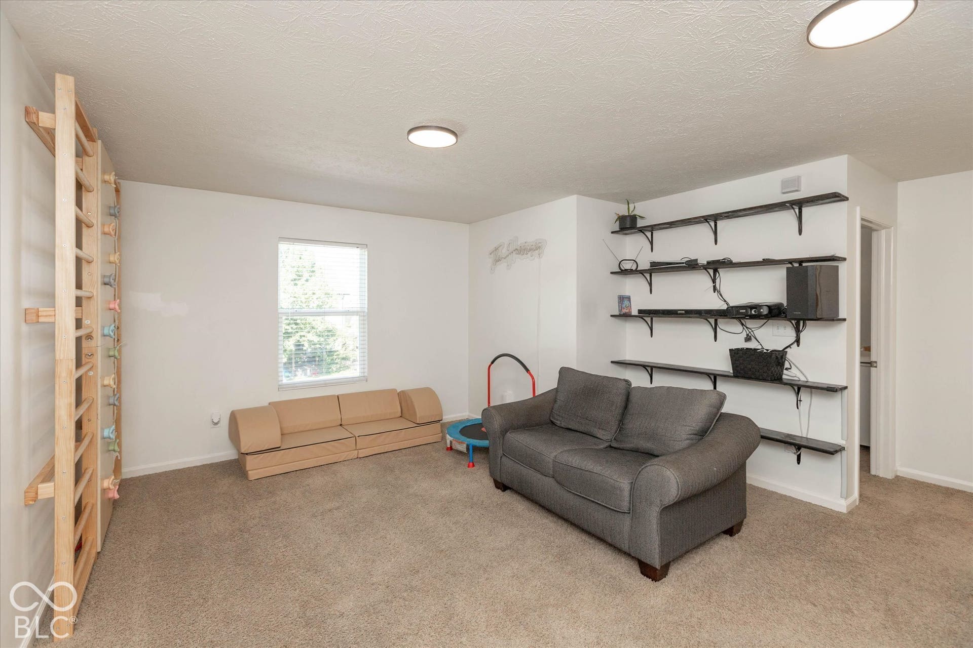 Recessed lighting, wall-mounted shelving, carpeted flooring, and a single window with blinds. Sellers will be keeping the jungle gym/climbing wall.