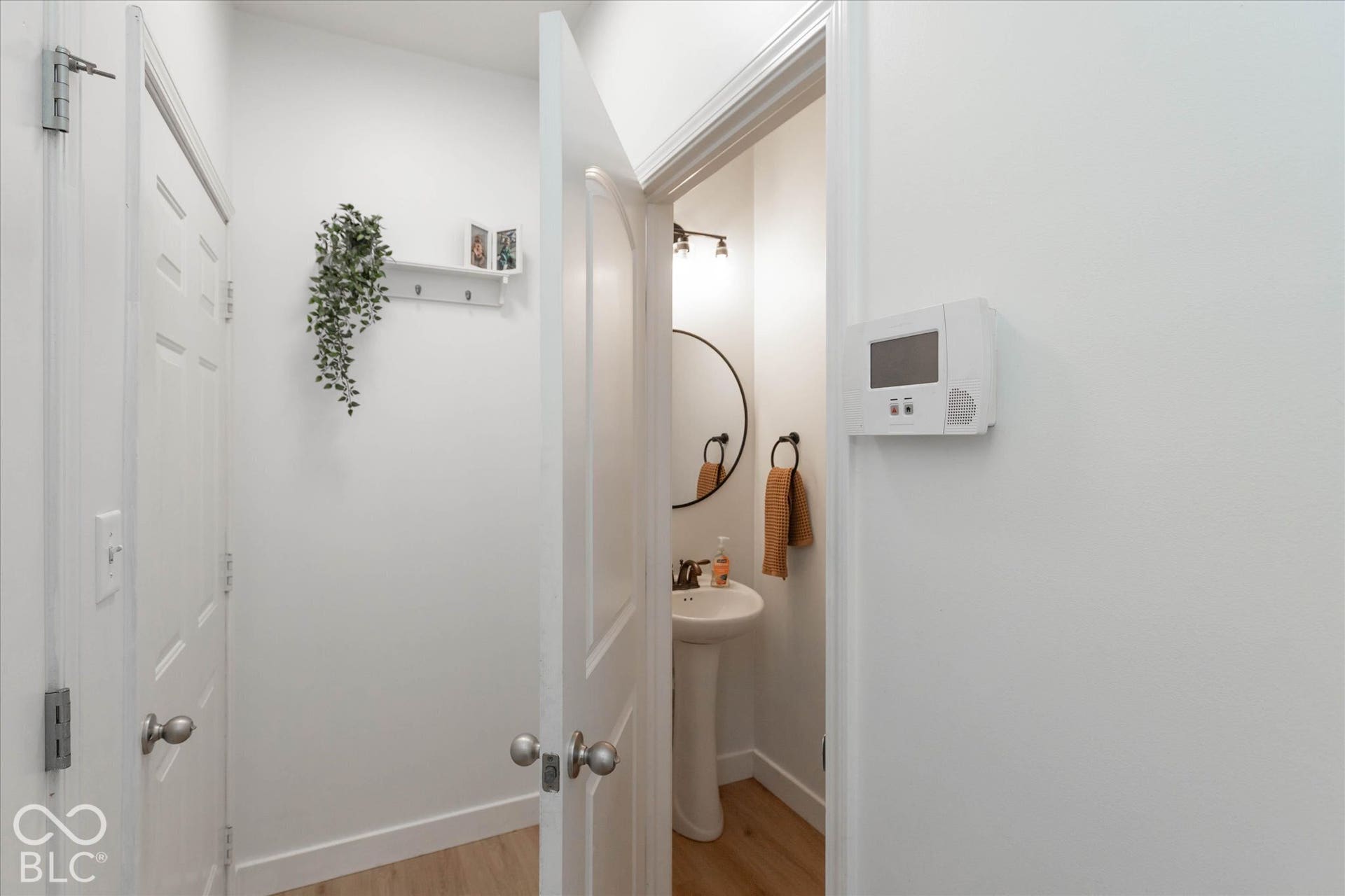 Pedestal sink with a circular mirror, bronze-finish wall-mounted light fixture, and wood-finish flooring