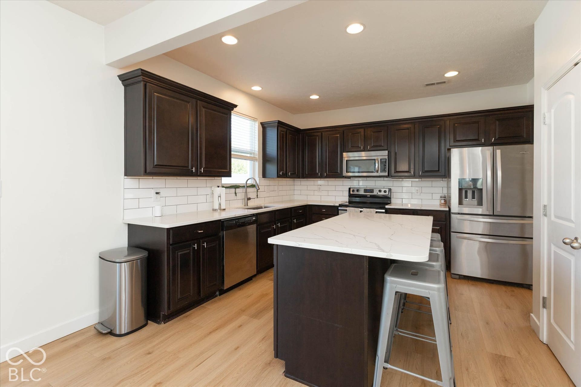 Kitchen featuring dark wood cabinetry, white quartz countertops, subway tile backsplash, and stainless steel appliances