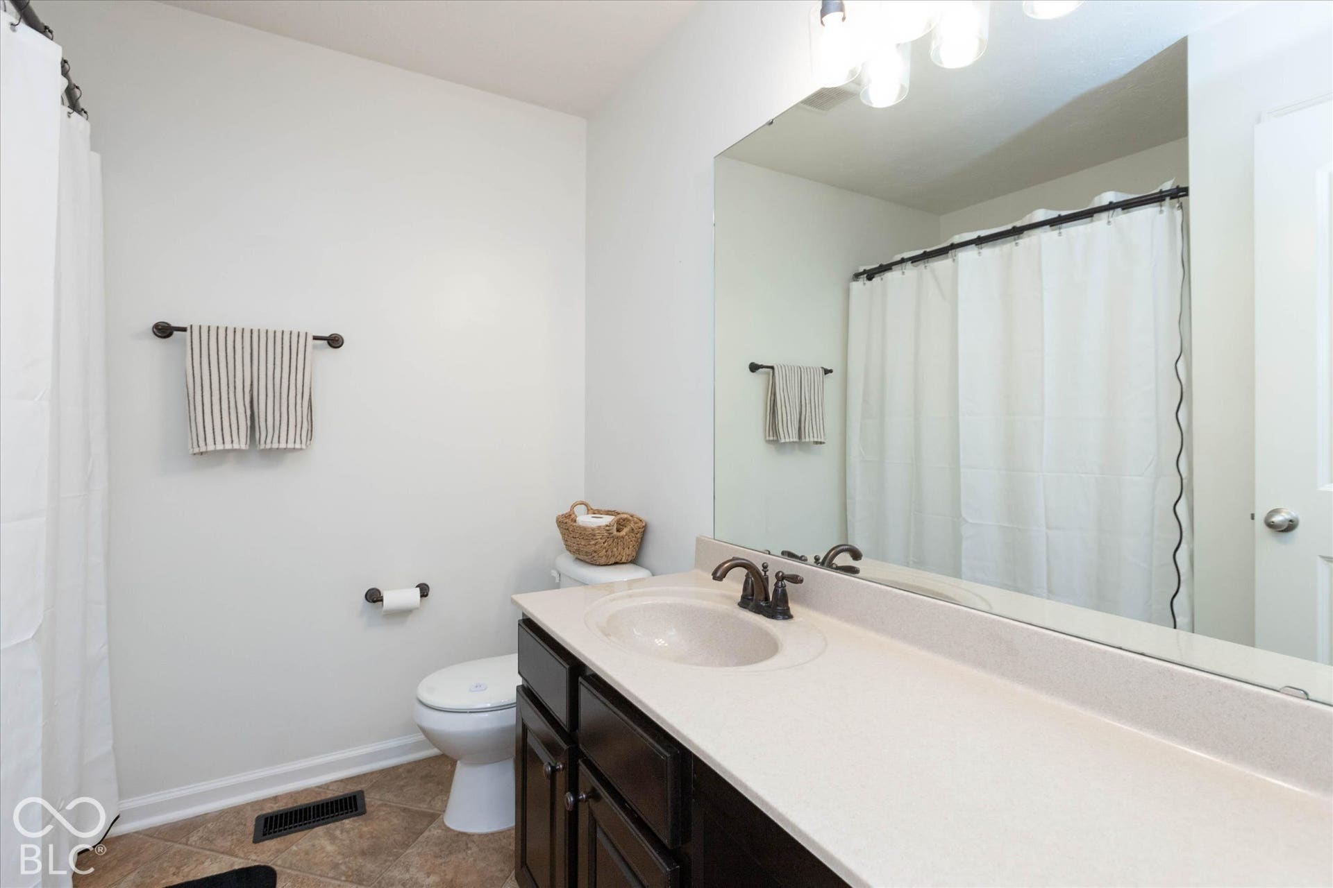 Upstairs Guest Bathroom featuring a dark wood vanity with a light-toned countertop, an integrated sink, and a large wall-mounted mirror
