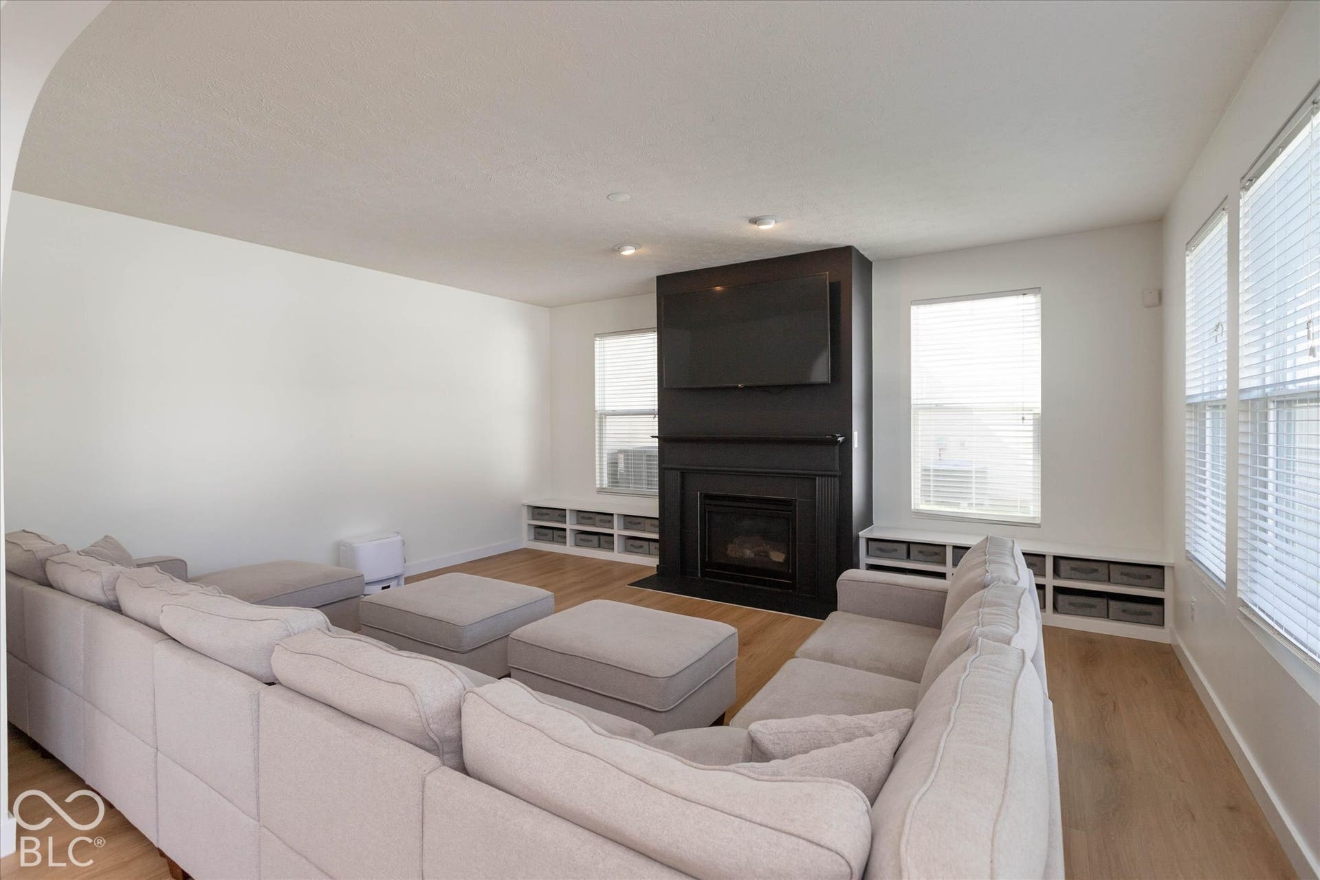 Dark-finished fireplace with an integrated media niche, light wood-finish flooring, white walls, multiple windows, and built-in lower cabinetry with storage cubbies