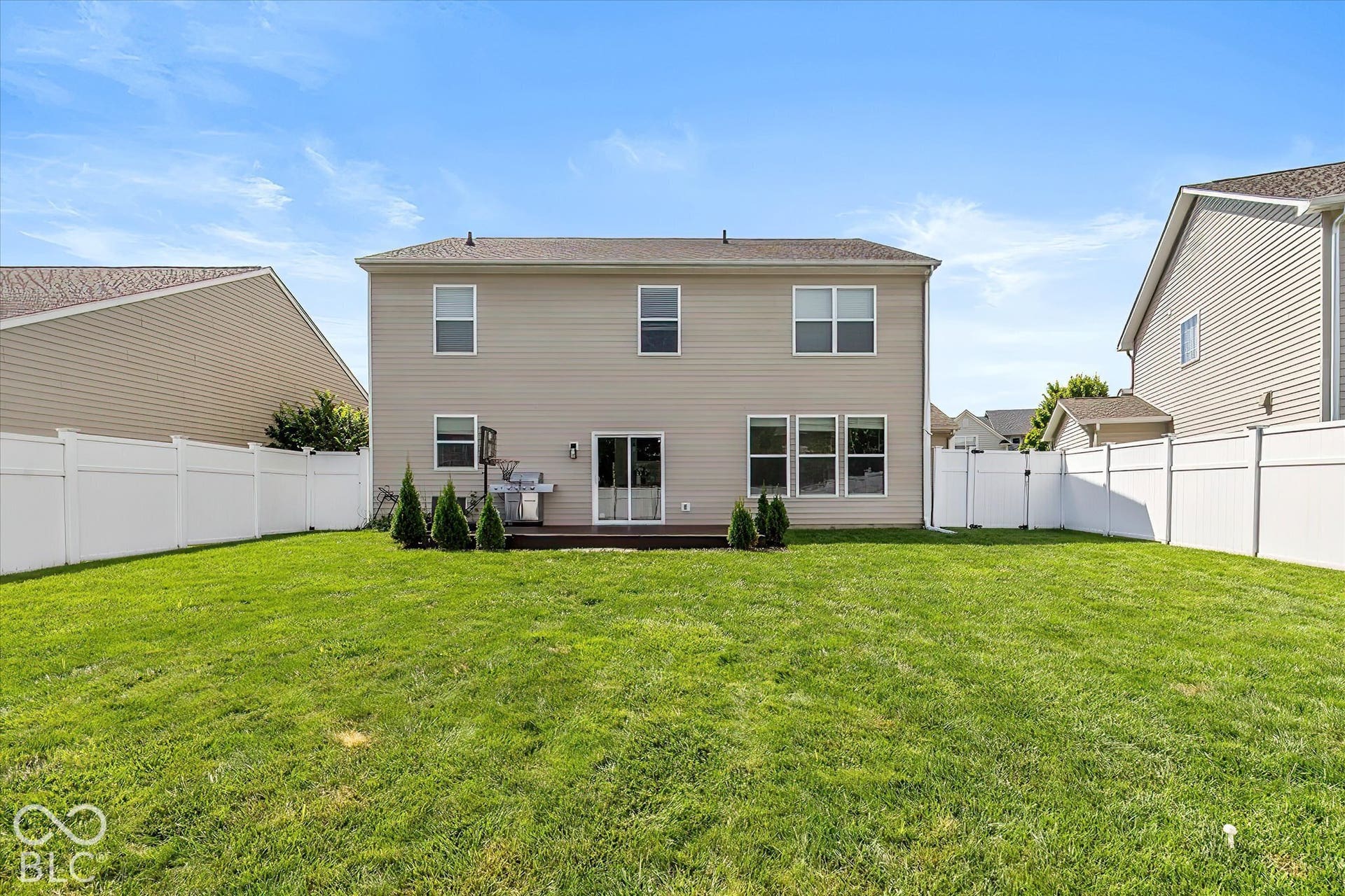 Expansive backyard with manicured lawn, full white privacy fencing, and a ground-level wood-finish deck