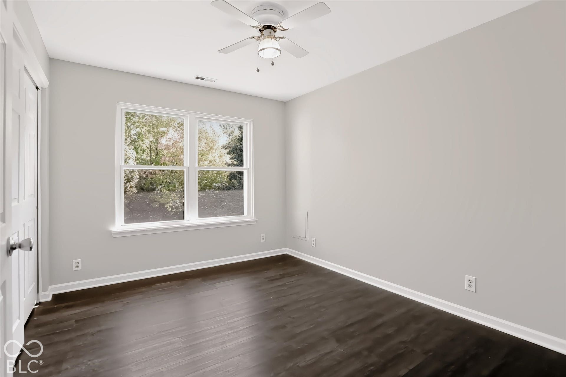 Dark wood-finish flooring, white walls, and a ceiling fan with integrated lighting