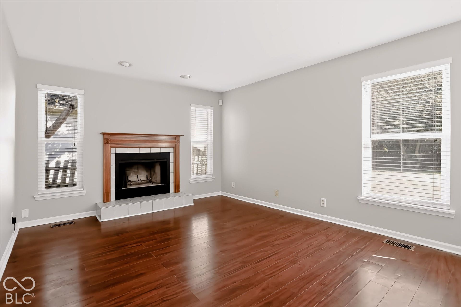 Wood-finish flooring with recessed lighting, a fireplace featuring a wood mantel, and multiple windows