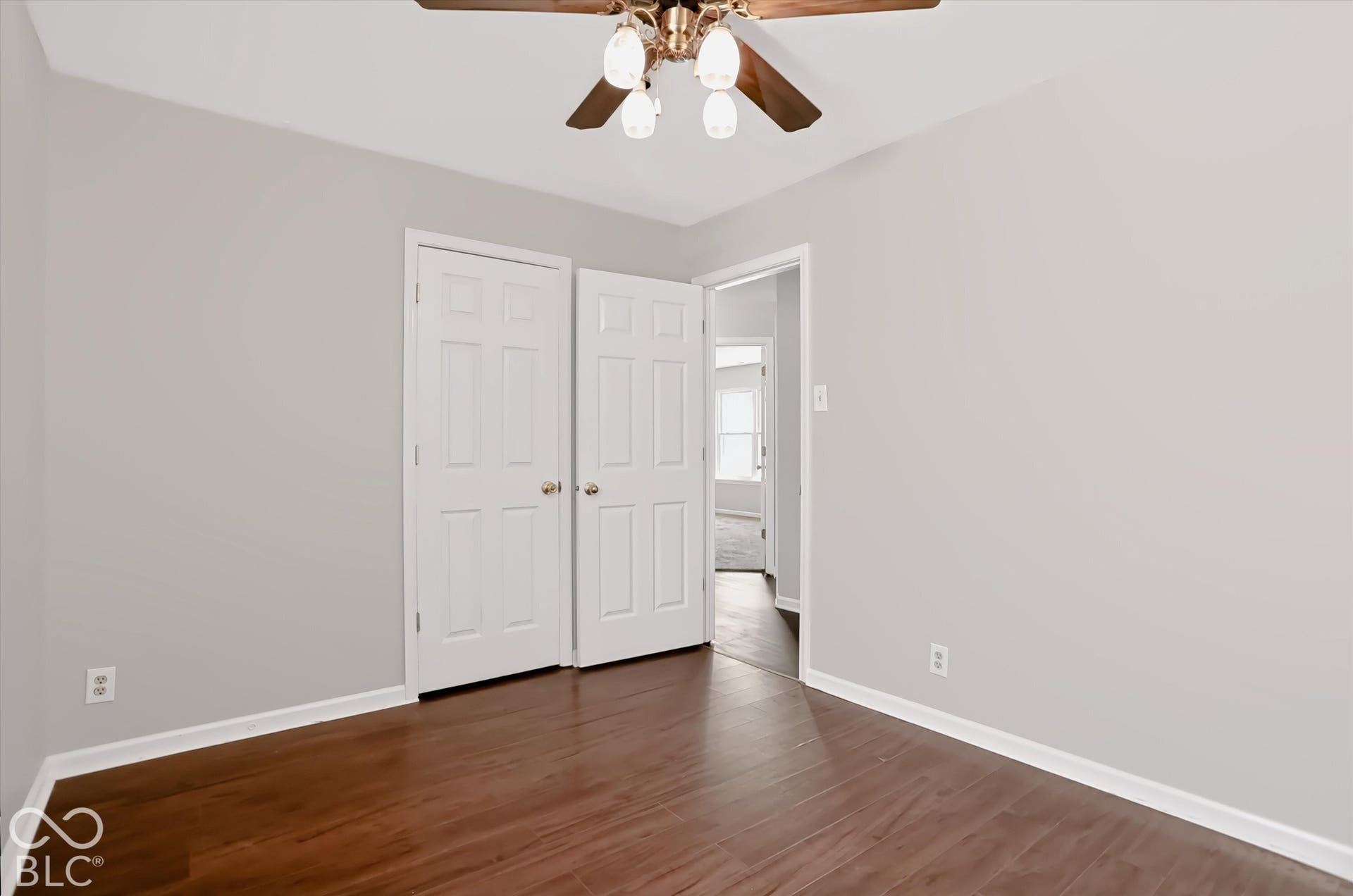 Virtually Altered - Wood-finish flooring with white baseboards, light neutral wall paint, and a ceiling fan with integrated lighting